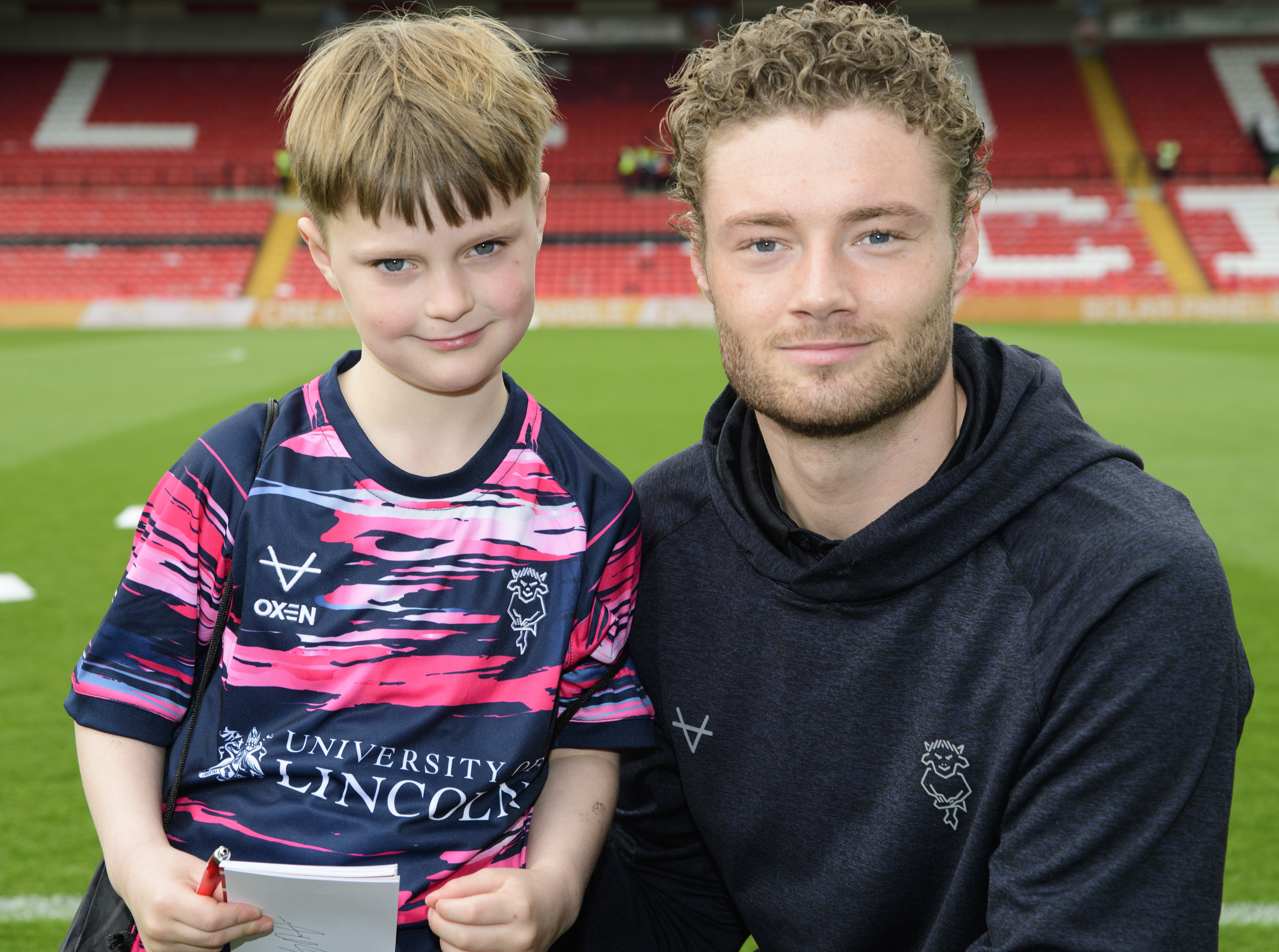 Lincoln City goalkeeper Lukas Jensen poses with a young fan, who is wearing a blue and pink replica shirt