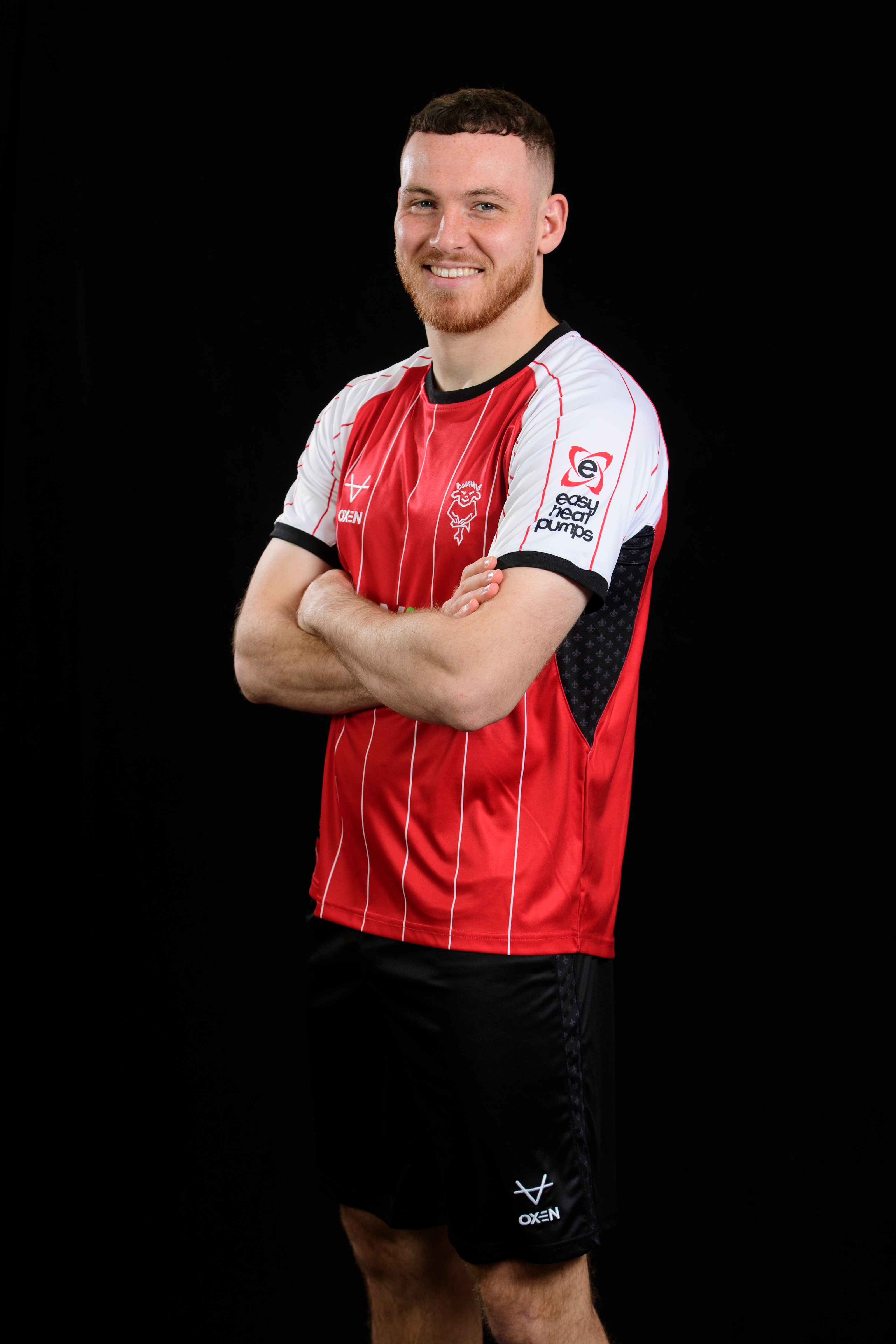 Ben House pictured wearing the 24/25 home kit. His arms are crossed and the Easy Heat Pumps logo is clear on the left arm.