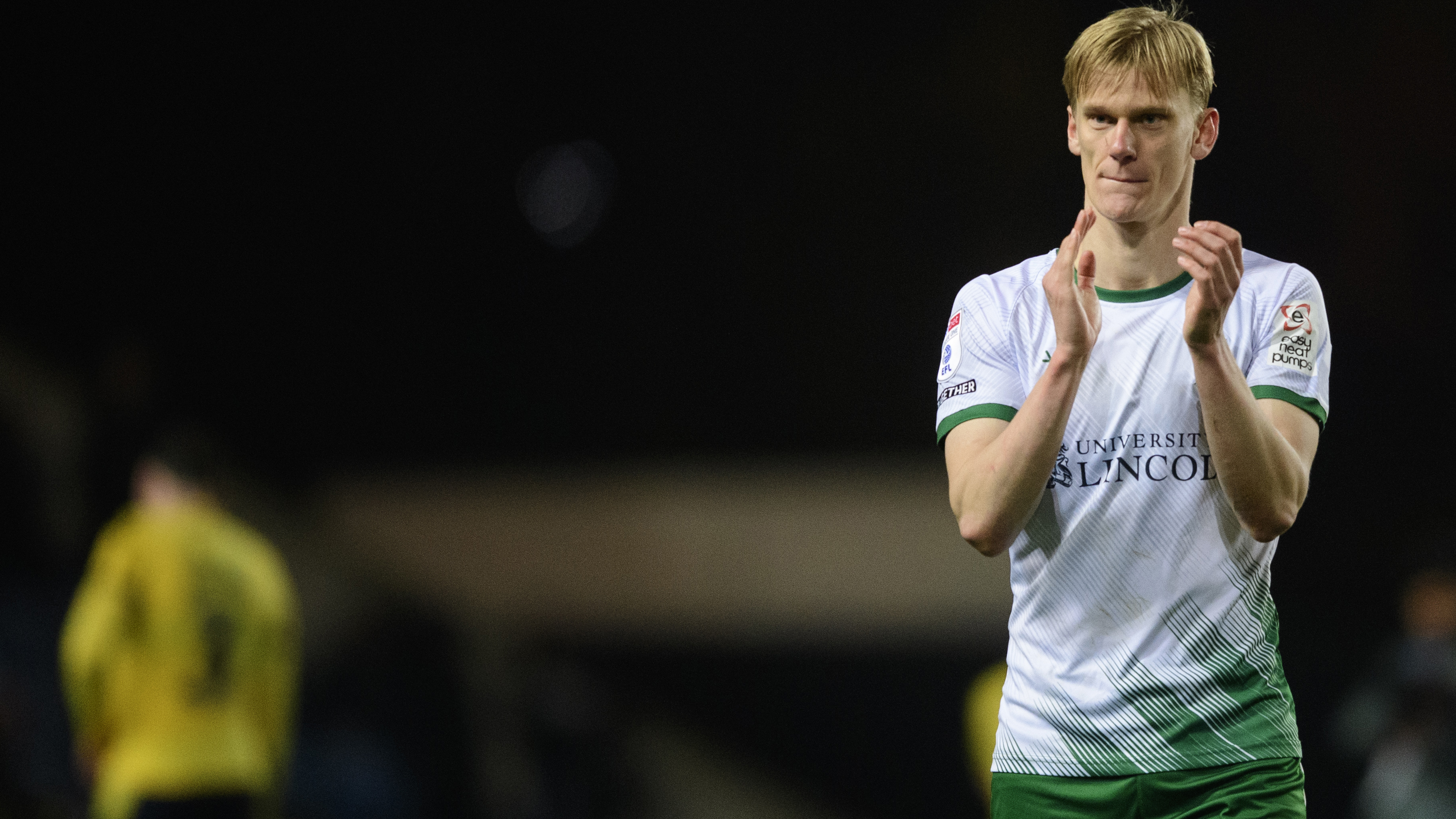 Lincoln City's Lasse Sorensen applauds after a match. He is wearing a white shirt and green shorts.