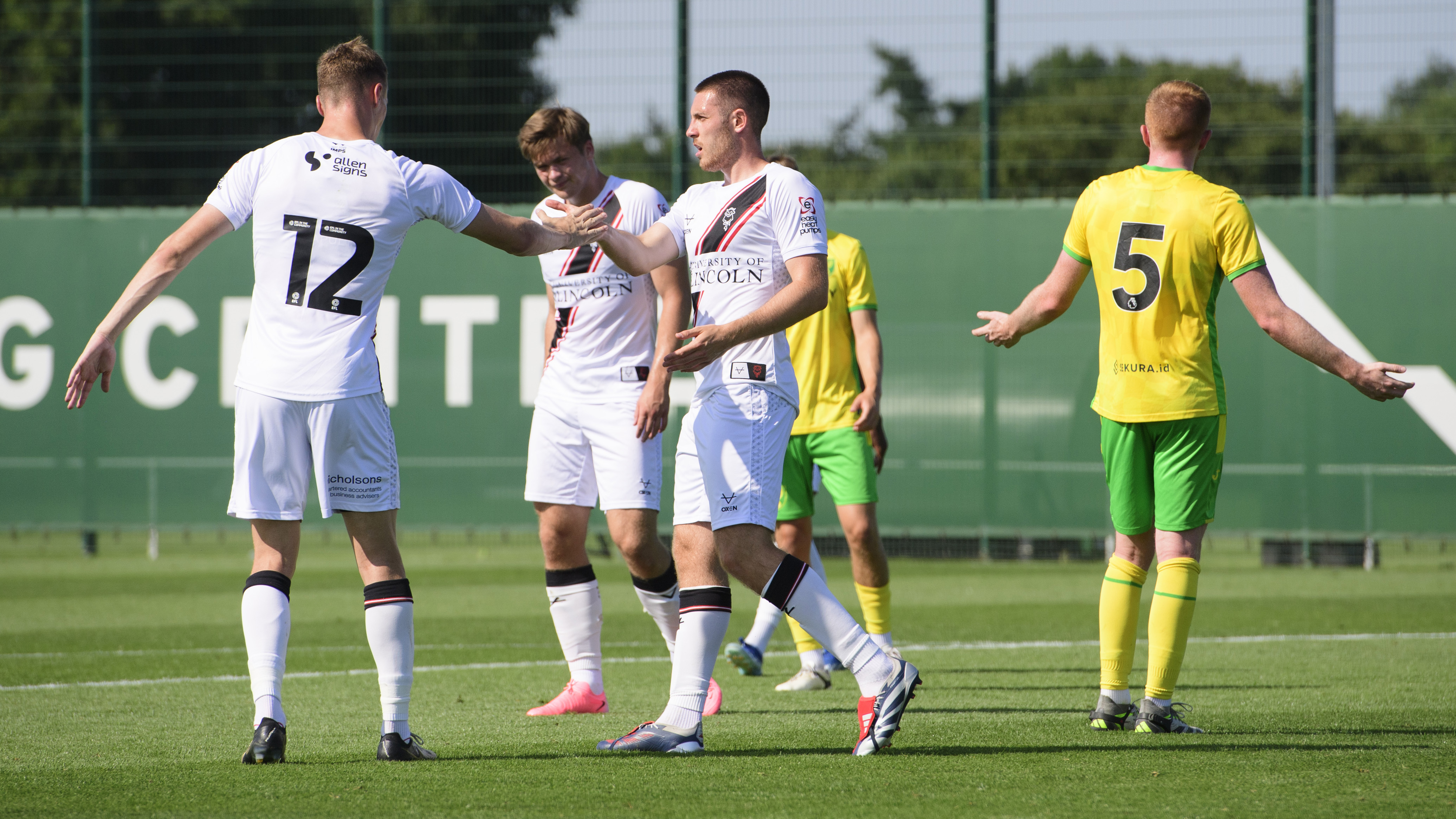 Two Lincoln City players congratulate Dom Jefferies (centre) after he scored. They are all wearing predominantly white football kit.