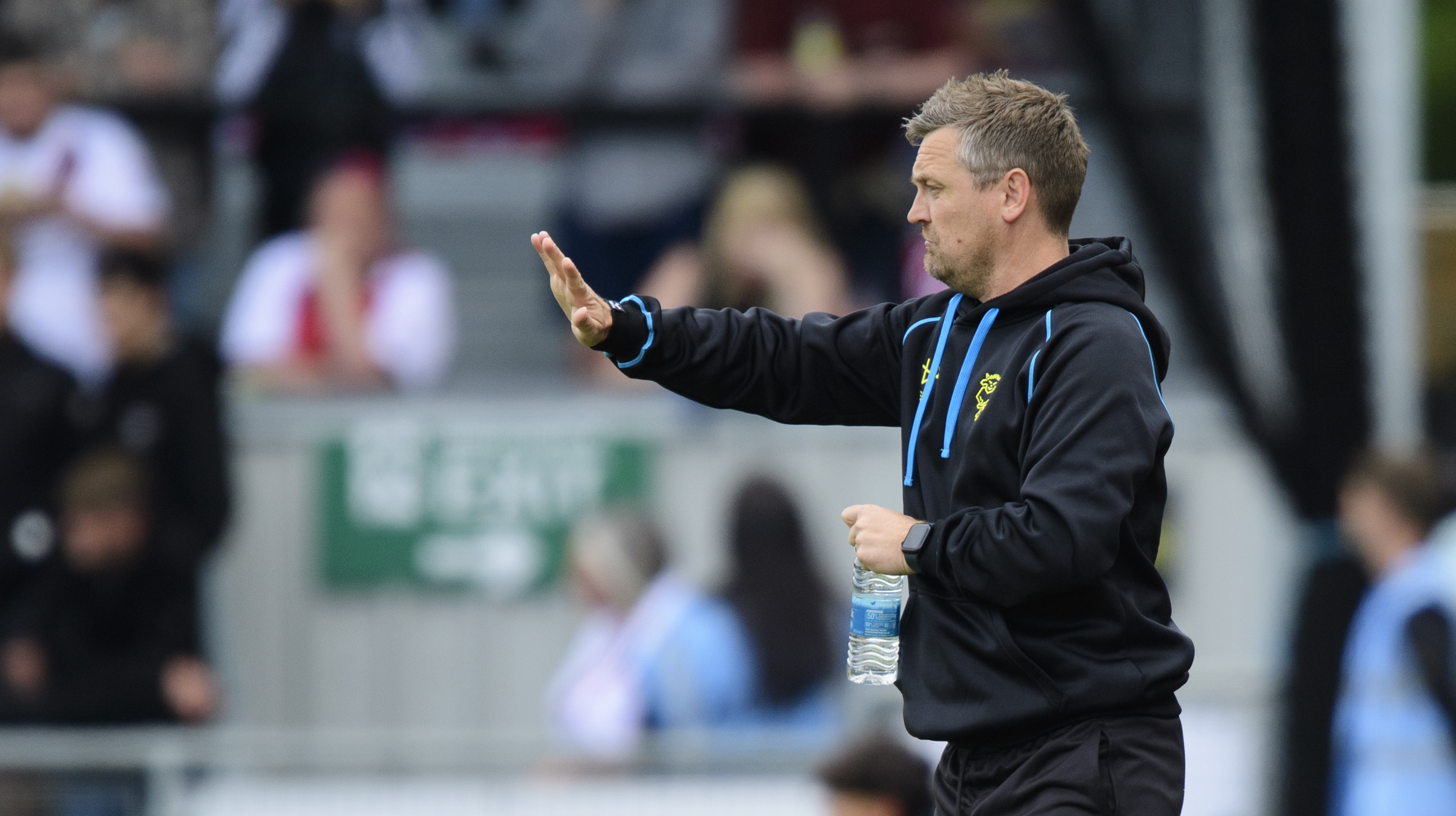 Lincoln City head coach Michael Skubala points during a match. He is wearing a black hoody.