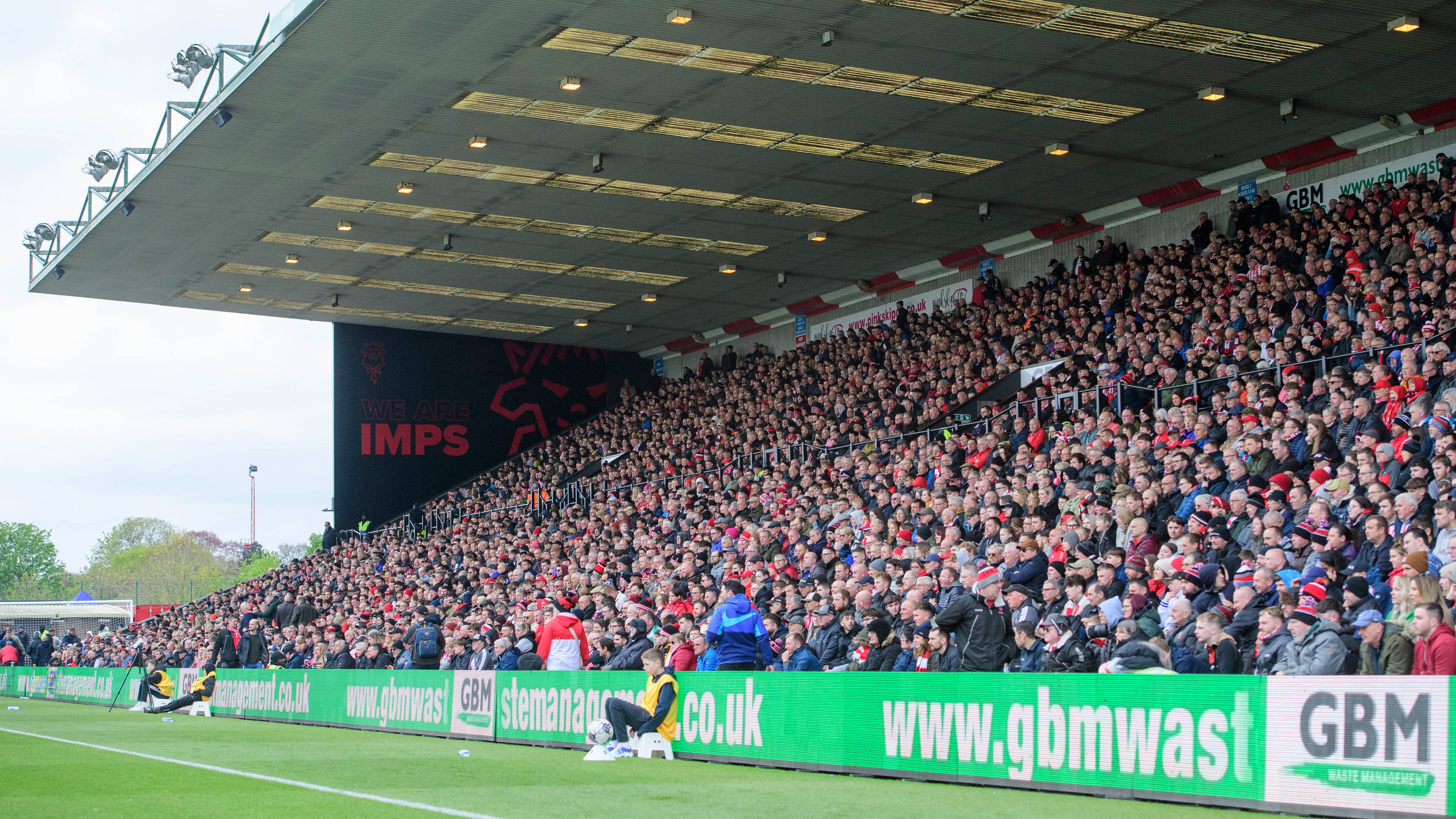Lincoln City fans pack out the GBM Stand during a game. a Mural at the end of the stand says "We Are Imps"