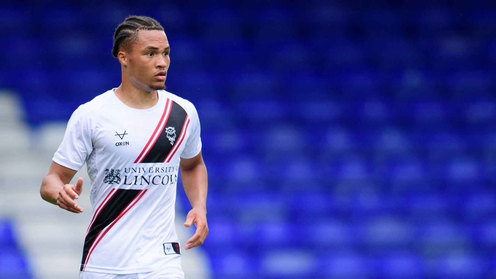 MJ Kamson-Kamara during a football match, he is wearing the white Lincoln City 24/25 away shirt