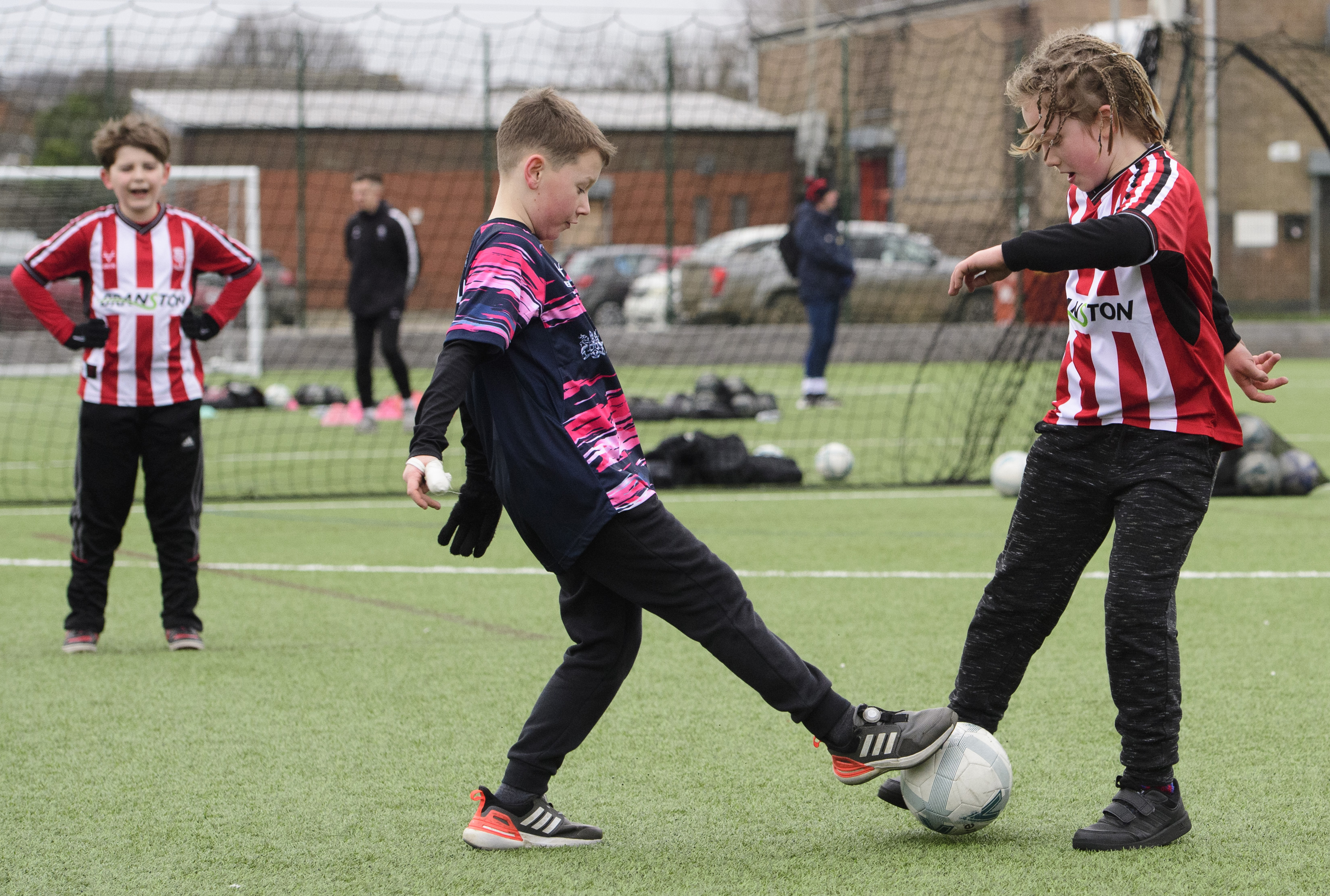 Two children challenge each other for the football on a 3G pitch. Both are wearing Lincoln City shirts