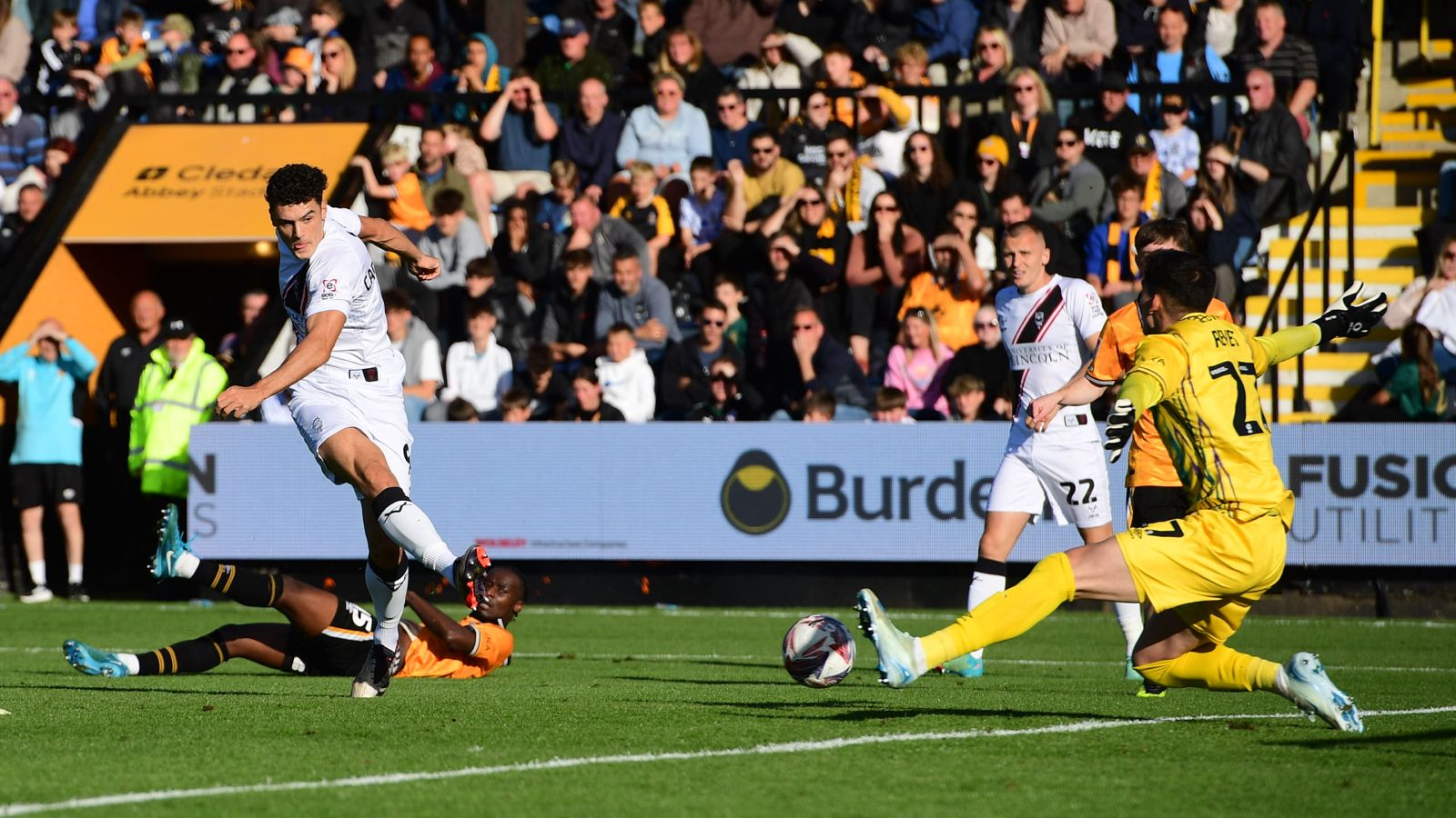 Bailey  scores his first goal for the club. He has shot with his right foot and the ball is about to go past the Cambridge goalkeeper.