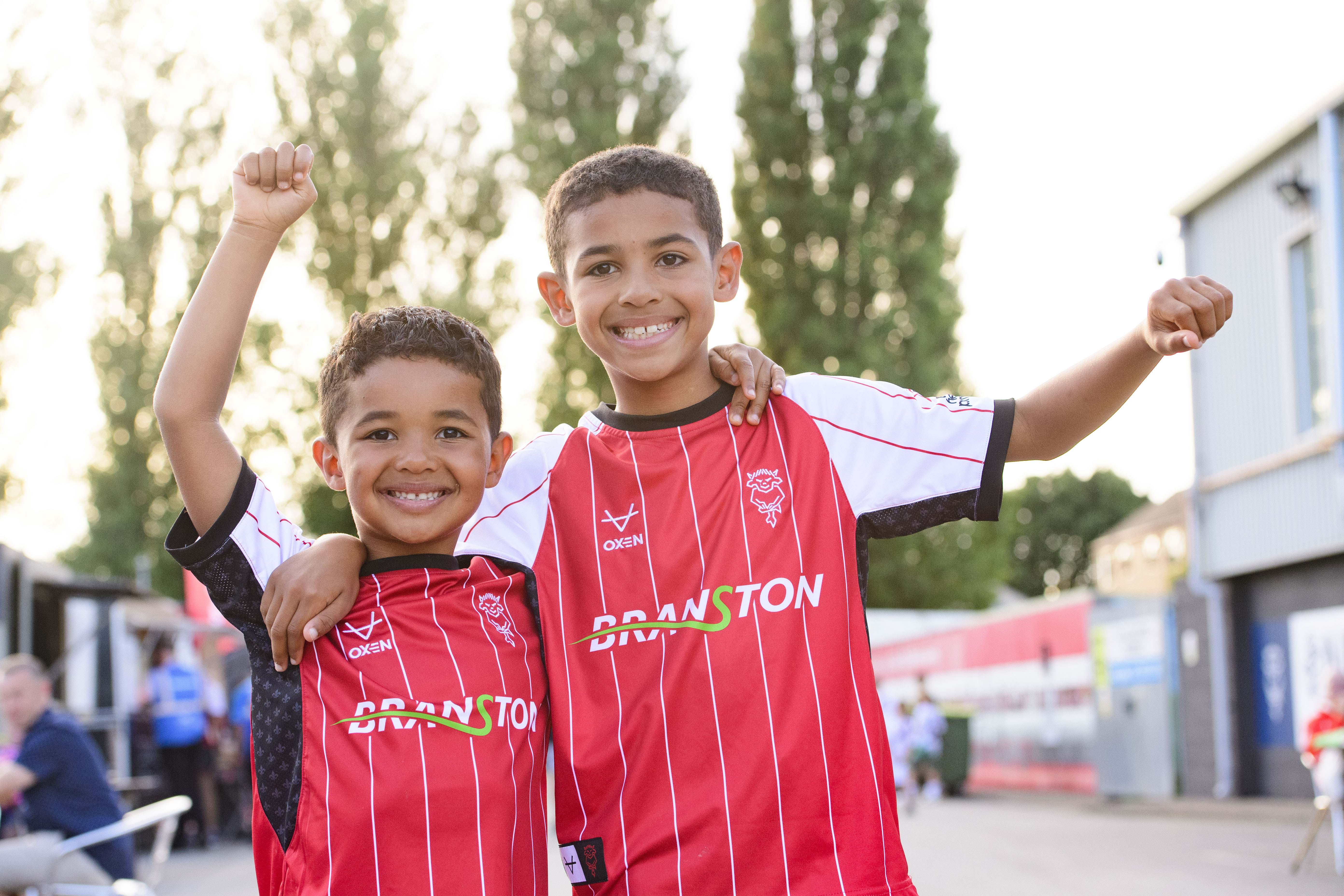 Two young boys cheer for the camera. They are both wearing red Lincoln CIty home shirts.