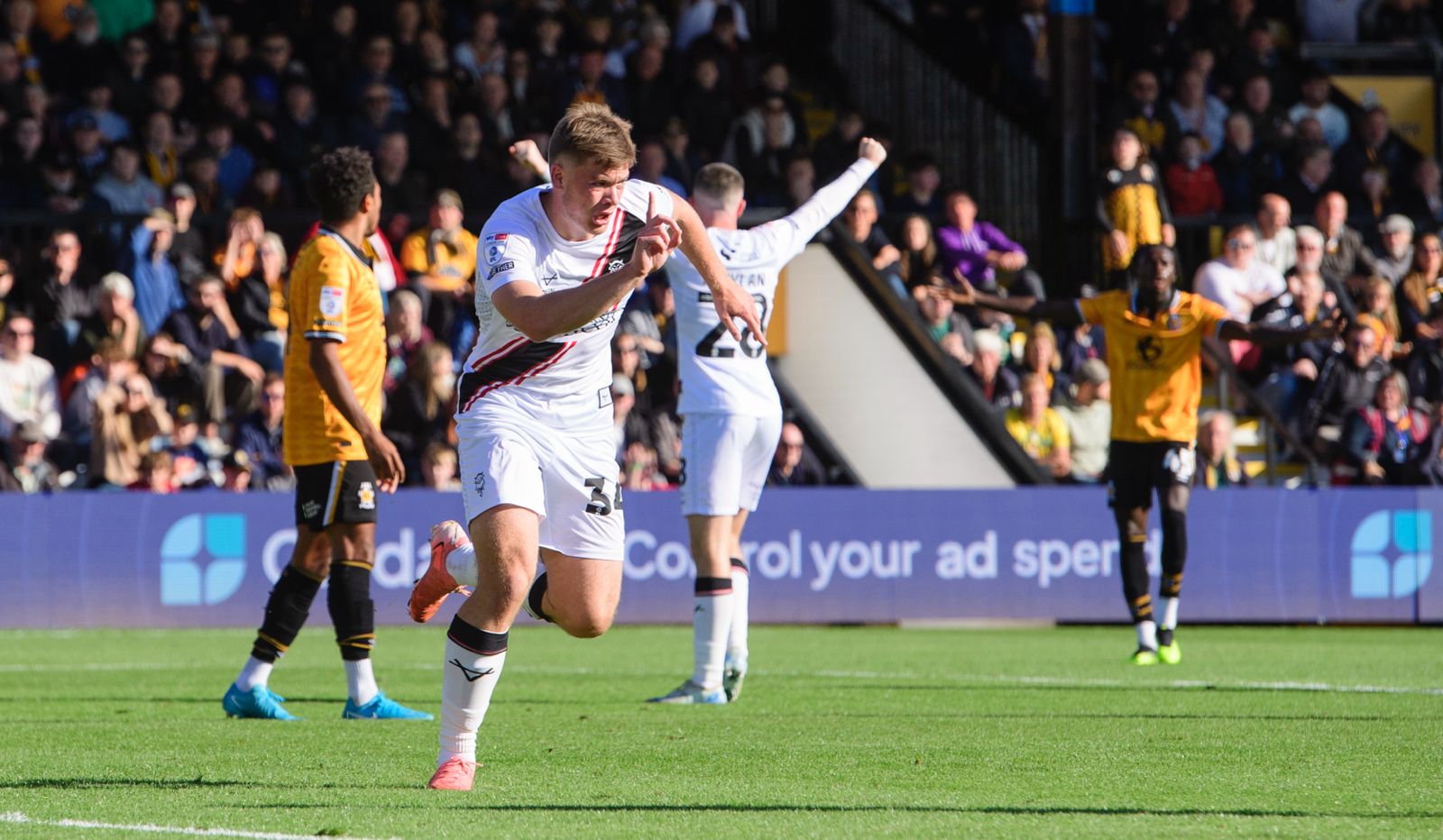 Freddie Draper runs off in celebration after scoring. He is holding his right hand up and pointing a finger.