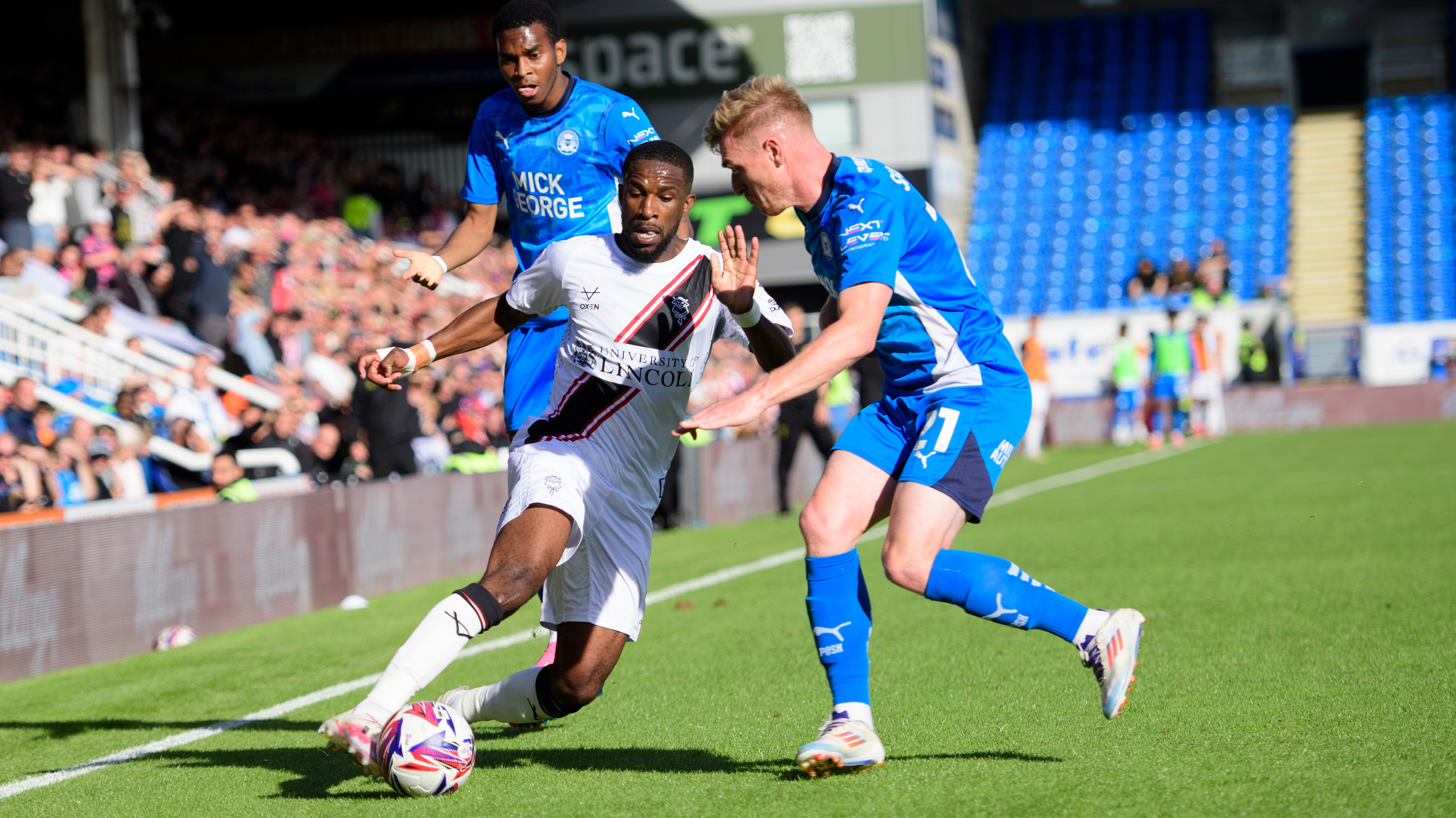 Tendayi Darikwa, wearing an all white kit, challenges for the ball with a Peterborough player wearing blue.