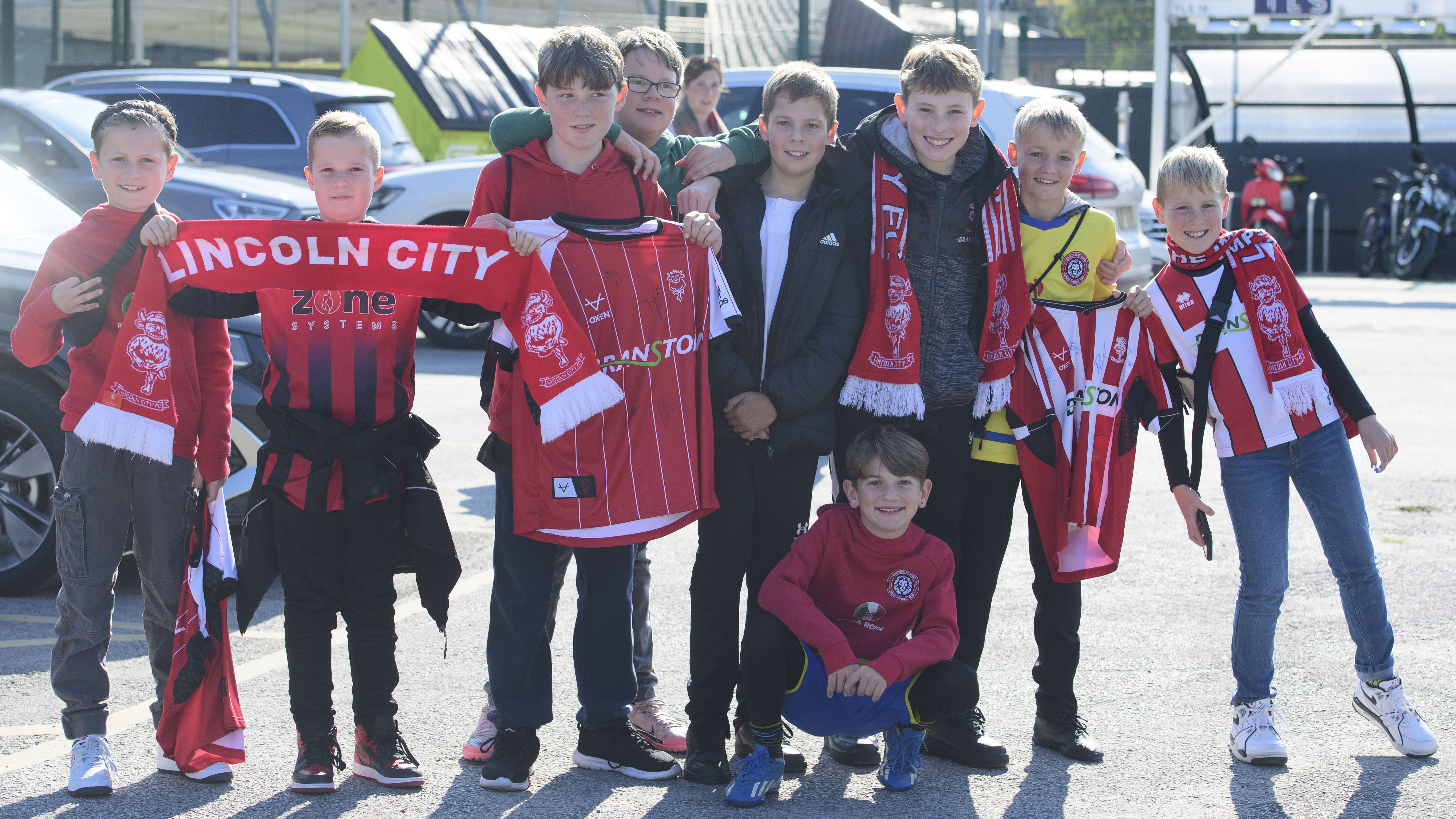 A group of children pose together, they are holding Lincoln City scarves and shirts