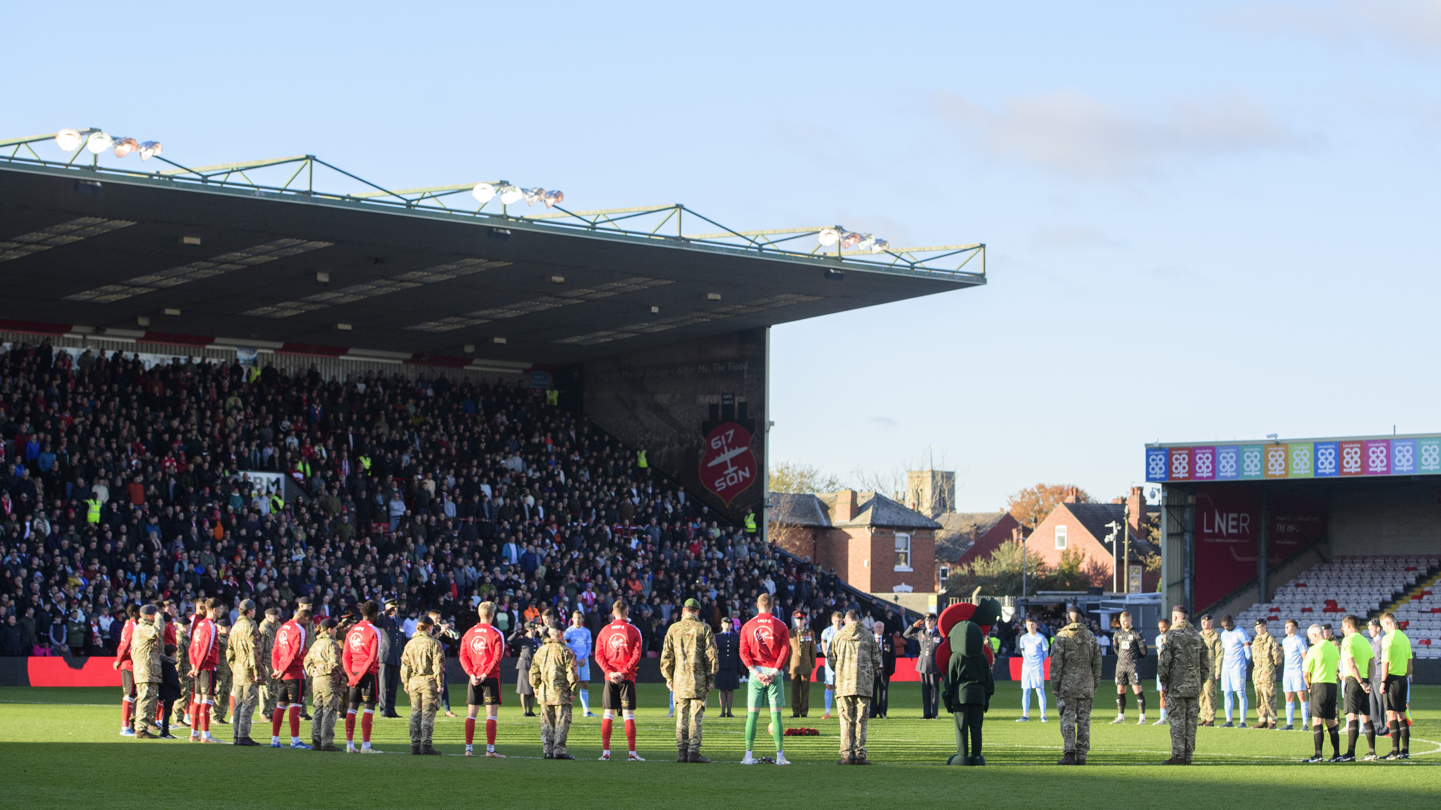 Footballers stand around the centre of a football pitch as part of a remembrance service at the LNER Stadium.