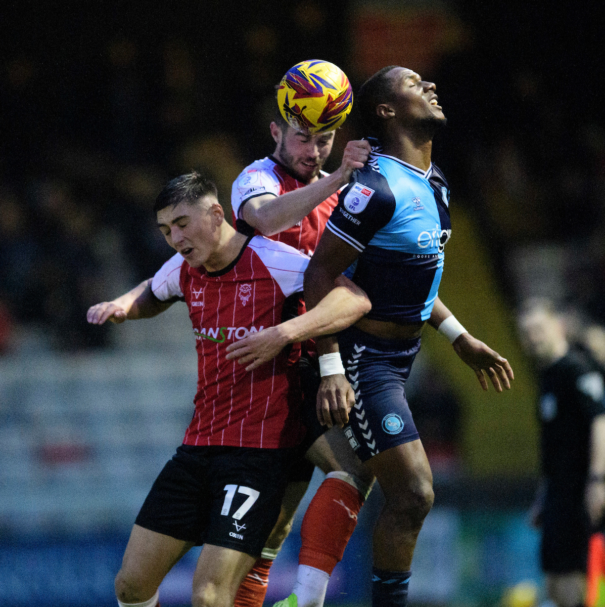 Dylan Duffy battles two Wycombe players in the air for the ball