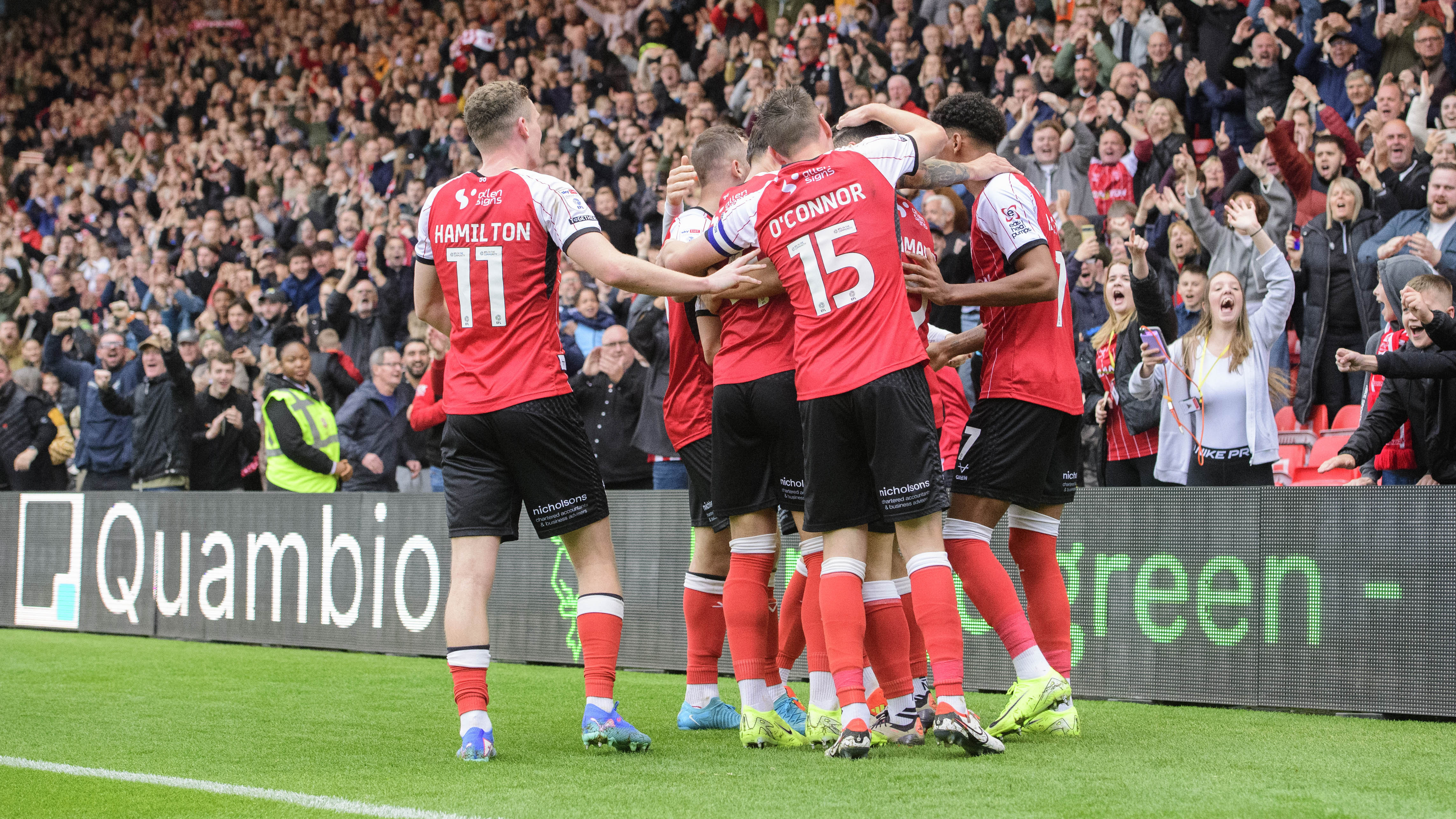 Lincoln City players celebrate a goal in front of a crowd of fans.