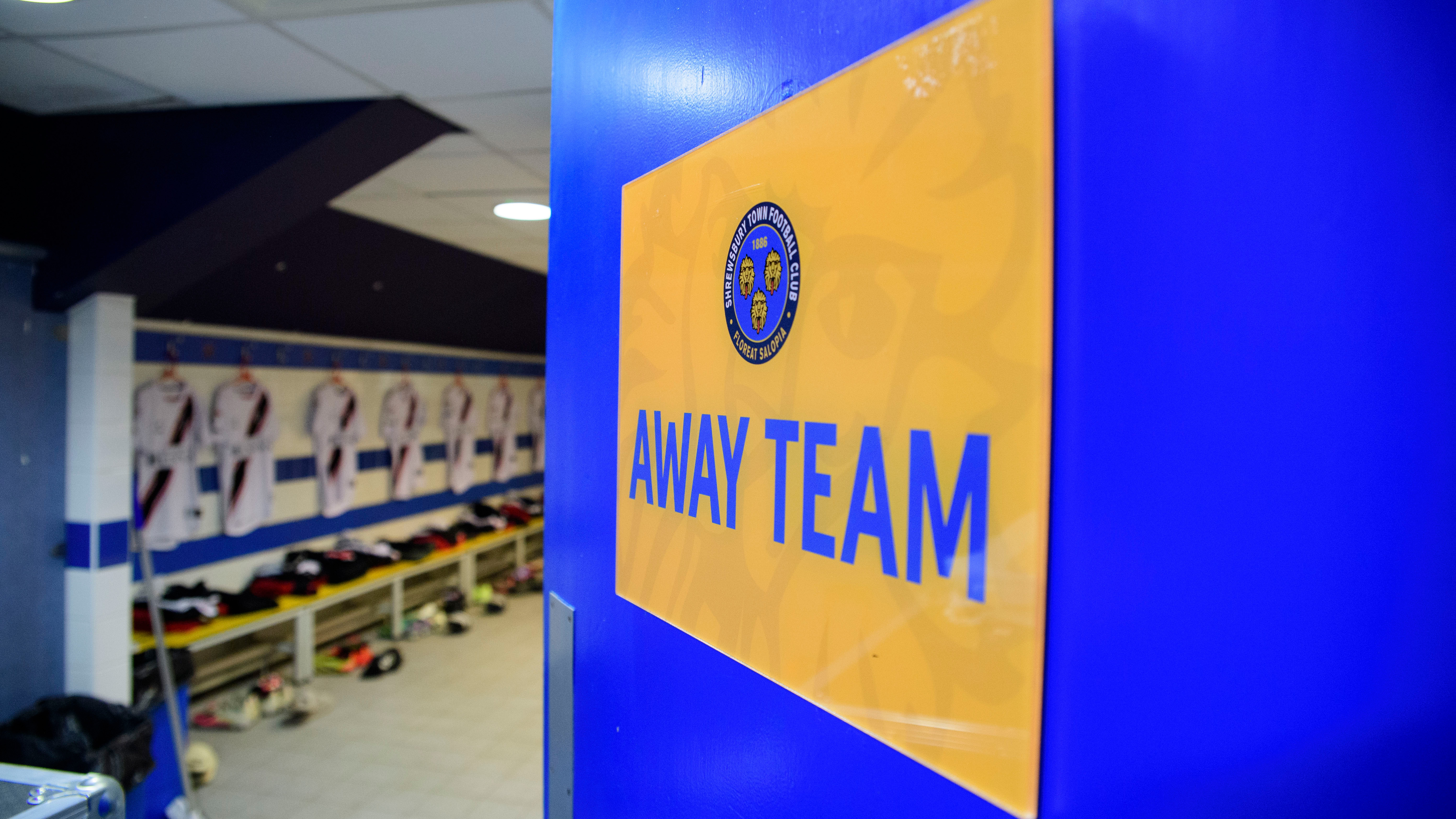 A sign which reads "away team" on a door looking into a football changing room