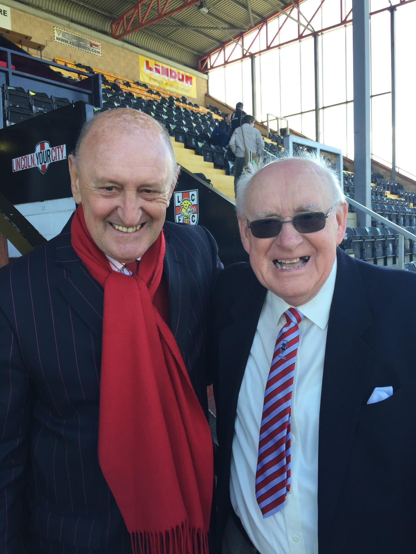 Former Lincoln City manager Colin Murphy poses for a photo with supporter Brian Baldam. They are stood at the front of a football stand.