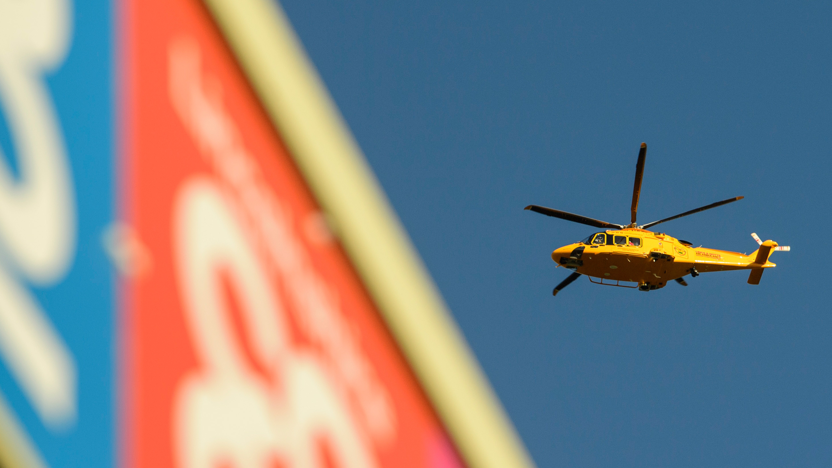 A yellow helicopter flies over a roof of the LNER Stadium. 