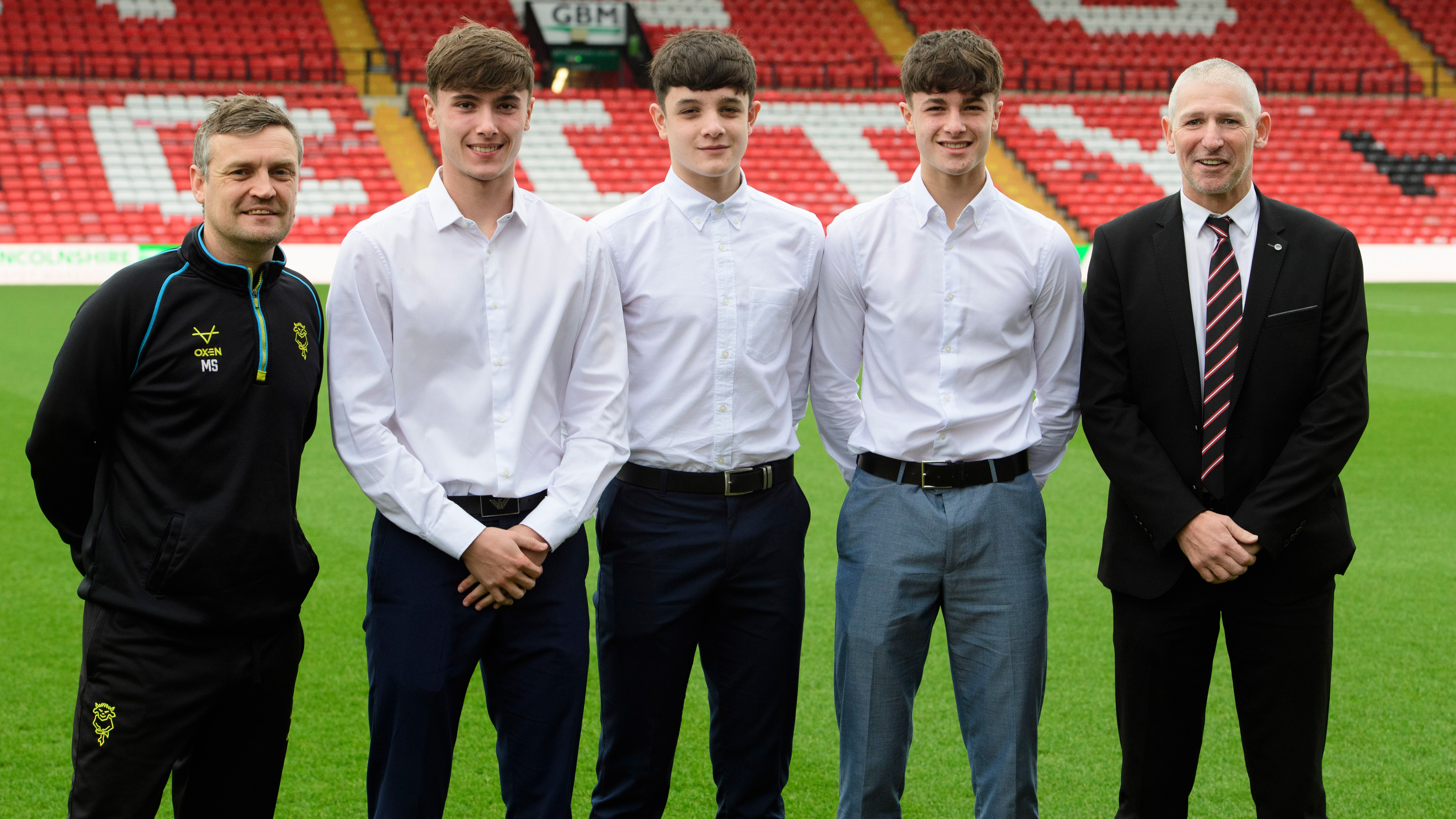 Five people stand in a line in front of a football pitch.