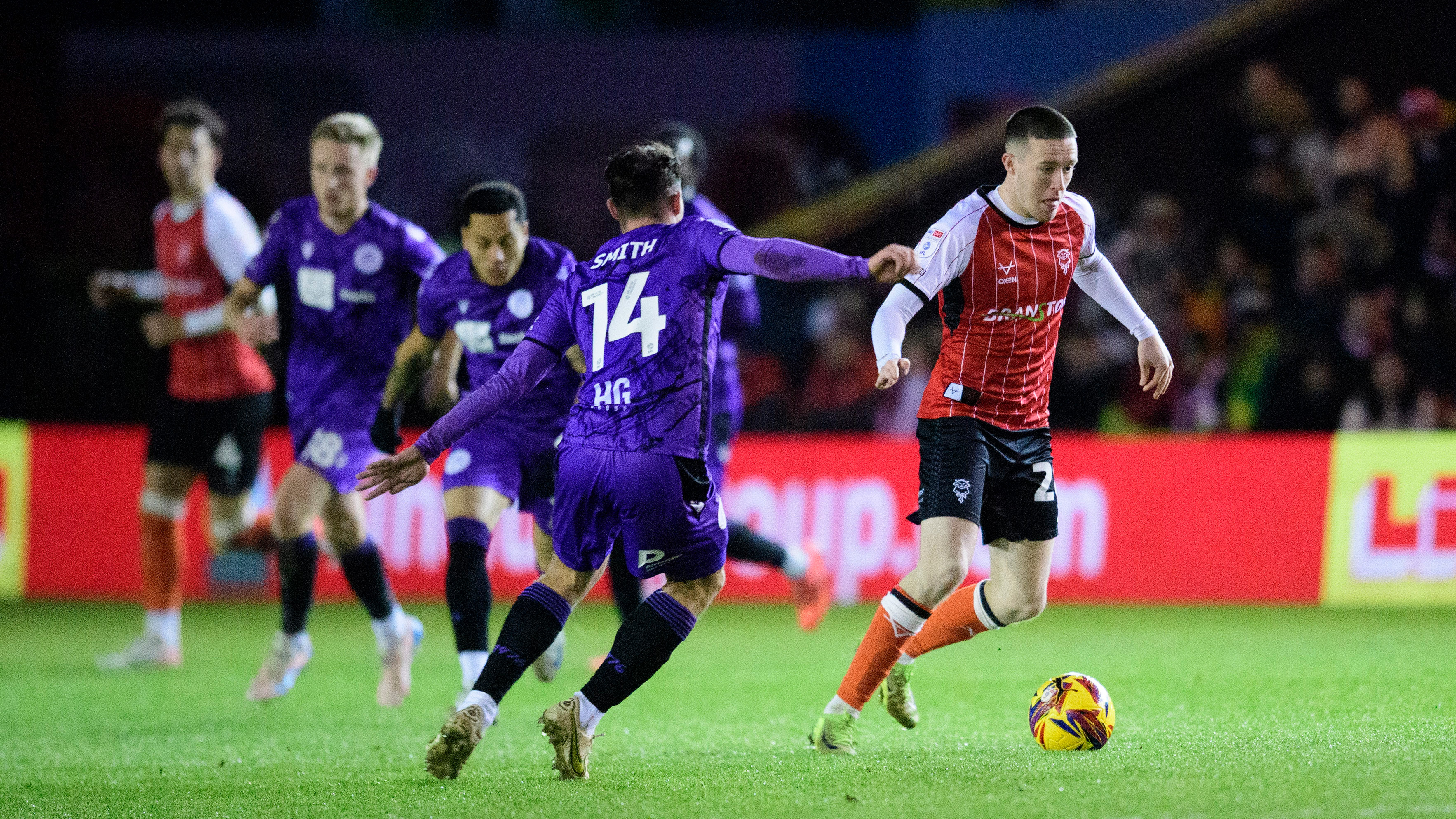 Jack Moylan, wearing a red home shirt, tries to get away from a Stevenage player wearing a purple kit