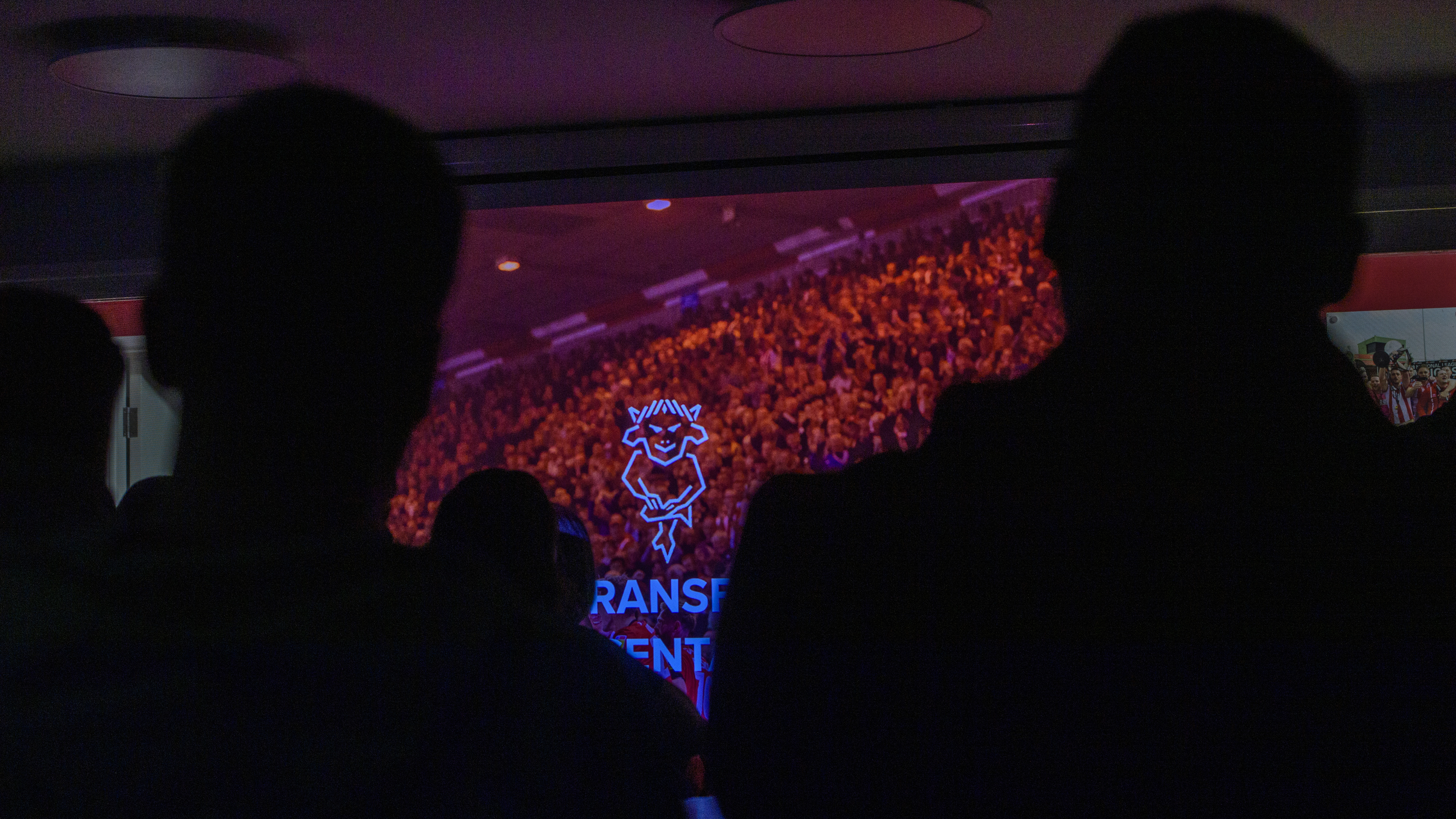 A graphic on a screen reads "transfer event". The room is darkened and there is a silhouette of two people in the foreground looking at the graphic.