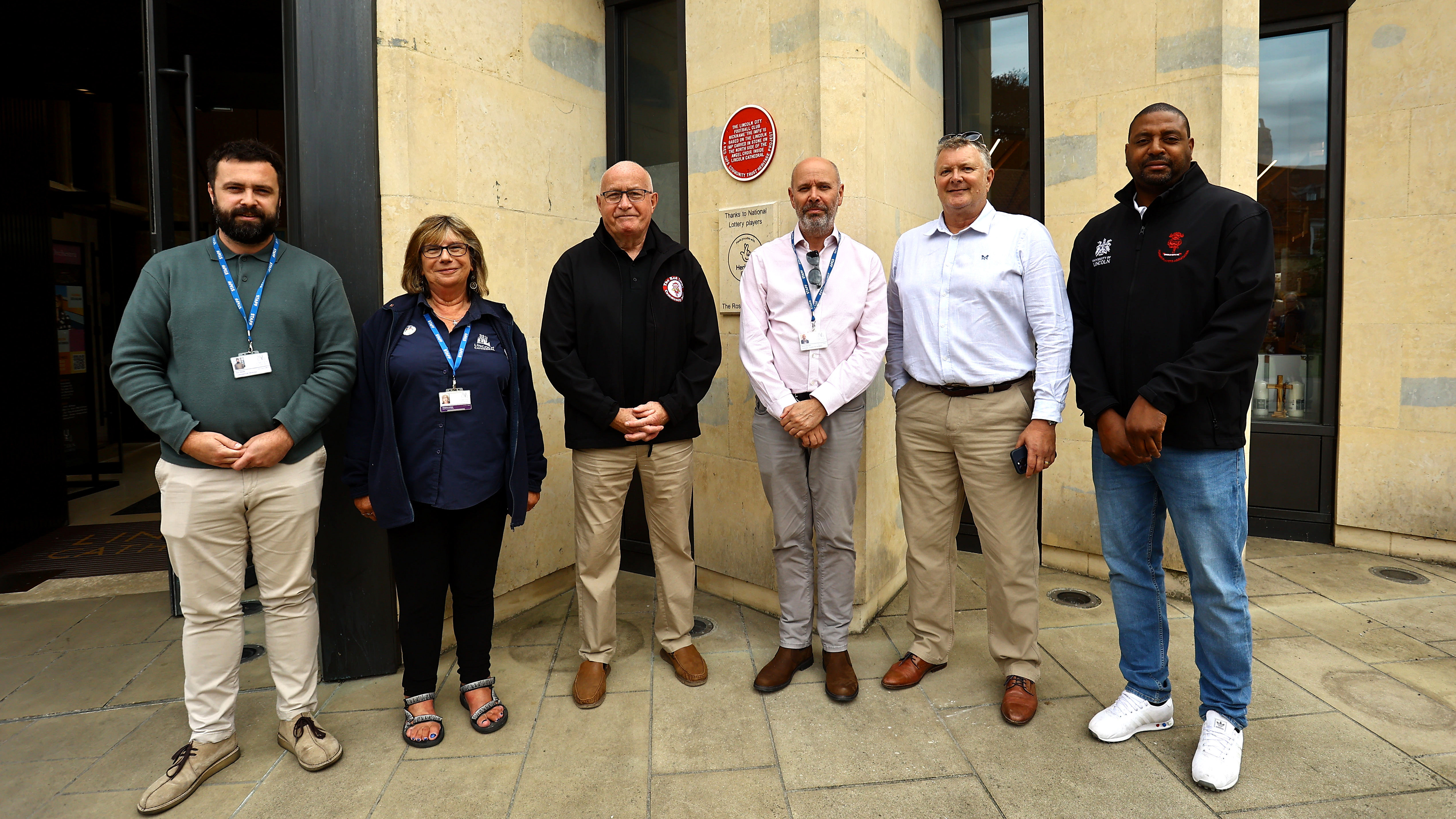 A group of people stand in front of a red heritage plaque.
