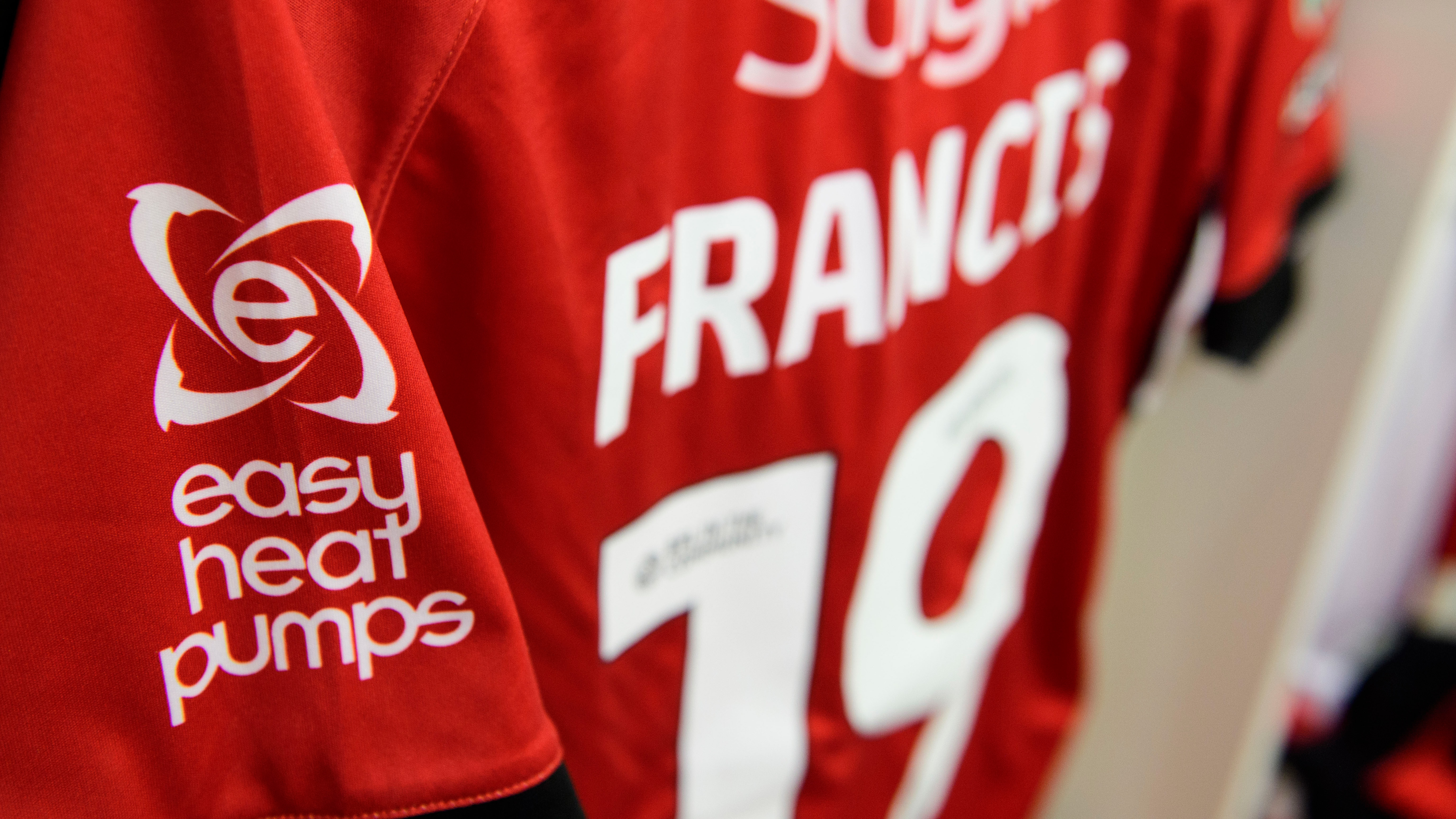 A close up of the Easy Heat Pumps logo on the sleeve of a red football shirt