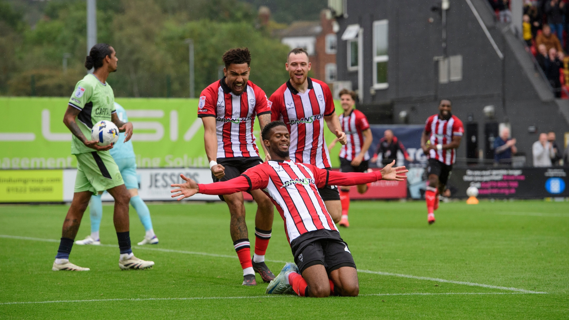 Justin Obikwu of Lincoln City, centre, celebrates scoring his side's second goal with team-mates Frankie Okoronkwo, left, and Ben House during the EFL Sky Bet League One match between Lincoln City and Luton Town at LNER Stadium, Lincolnshire.