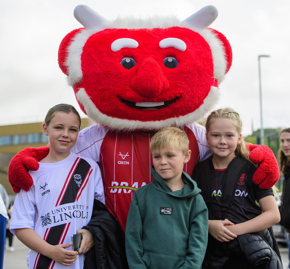 Poacher the Imp poses for a photo with three young Lincoln City supporters