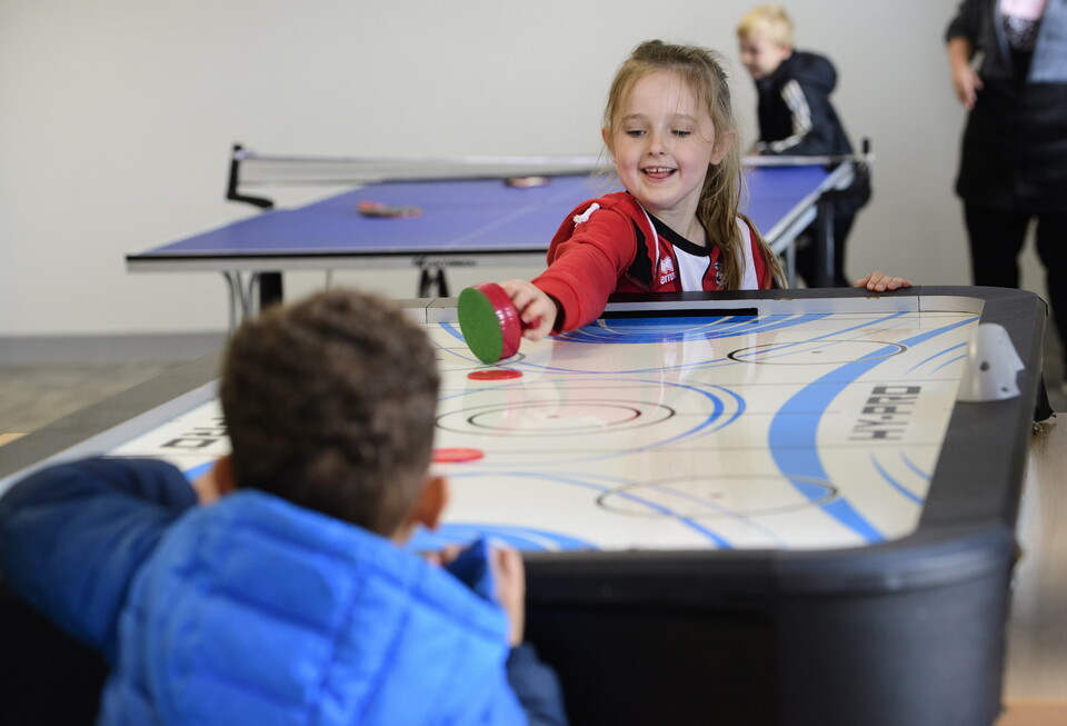 Two children play a game of air hockey in the Co-Op Community Hub