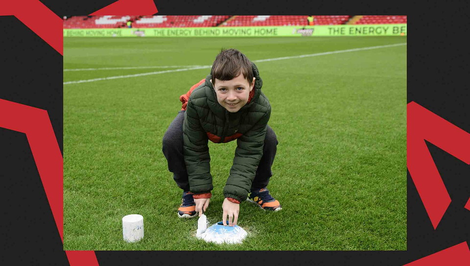 A child paints a penalty spot on a football pitch