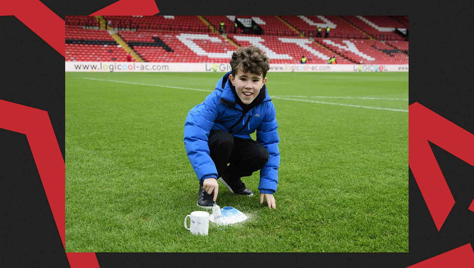 A child paints a penalty spot on a football pitch