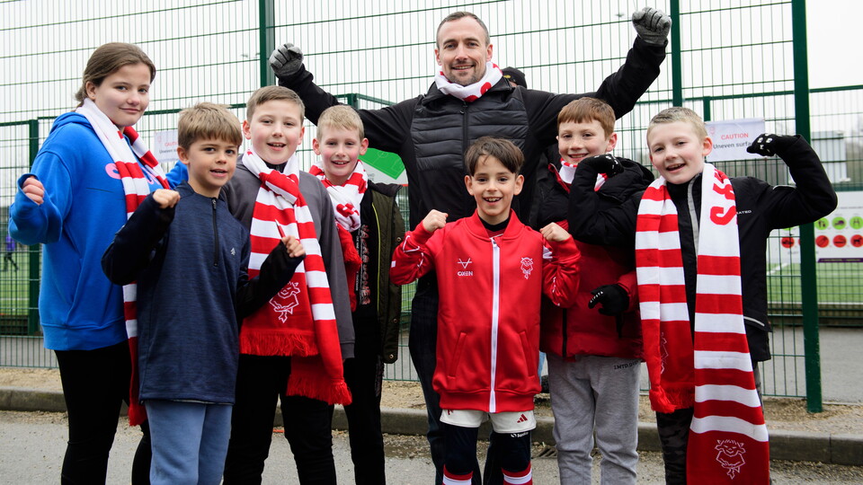 A group of Lincoln City supporters pose for a photo. They are all raising their aims in celebration.
