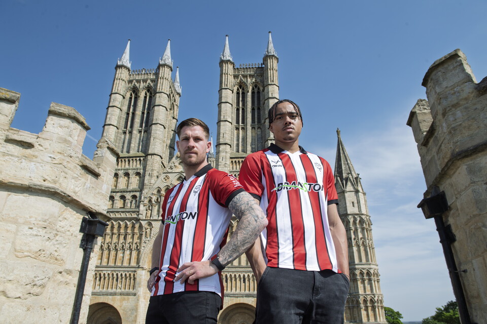 James Collins and Jovon Makama wear red and white shirts in front of Lincoln Cathedral