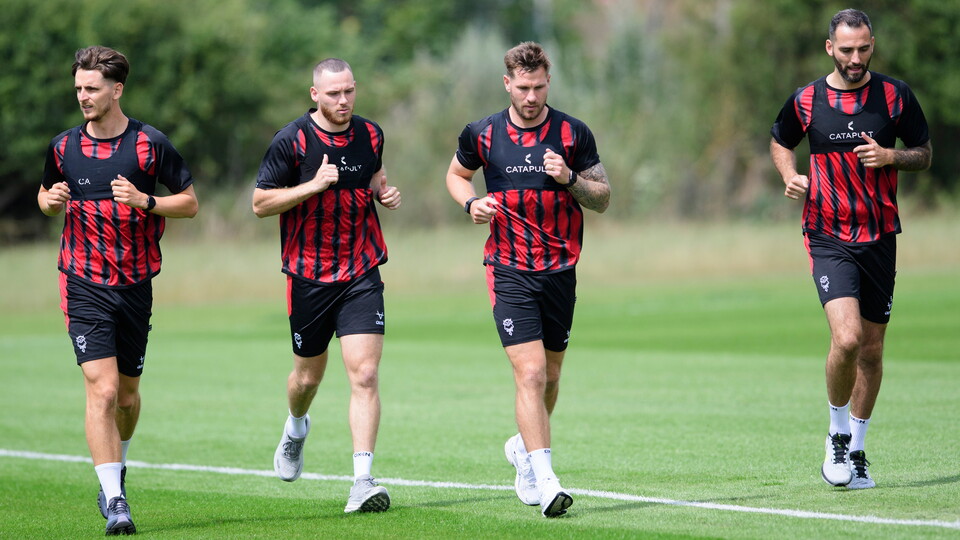 Four players in dark red and black tops run on grass
