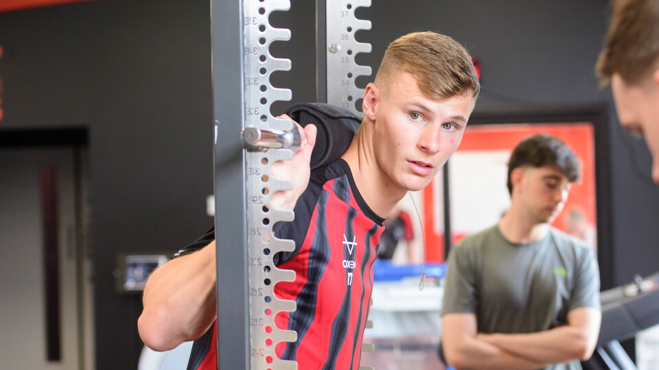 A man pushes his back against a bar in a gym.