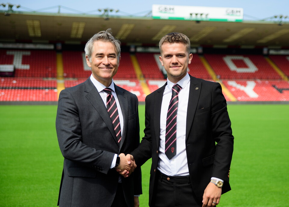 Two men stand in suits shaking hands.