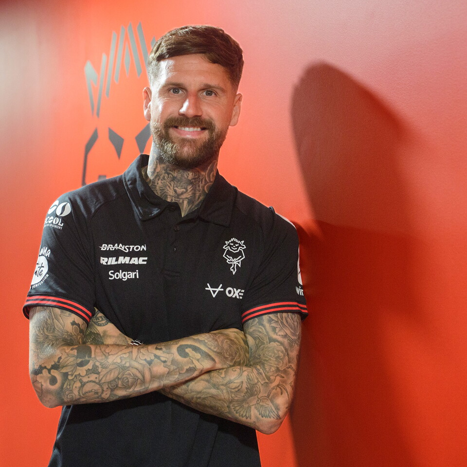 Sonny Bradley poses in a black polo top against a red wall