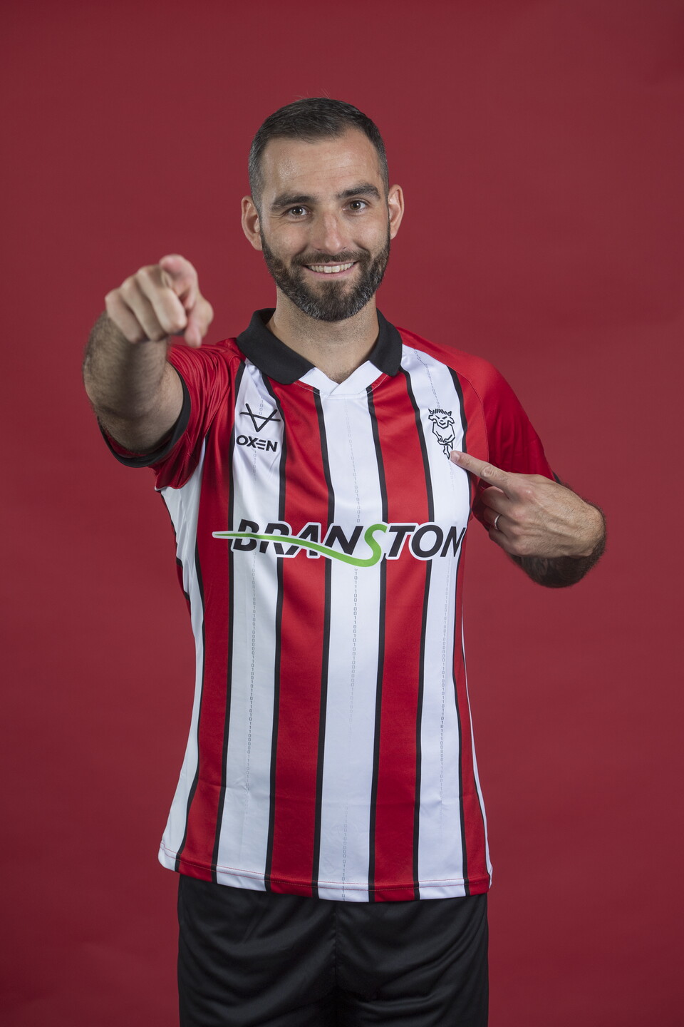 Adam Jackson points to the badge on his Lincoln City shirt