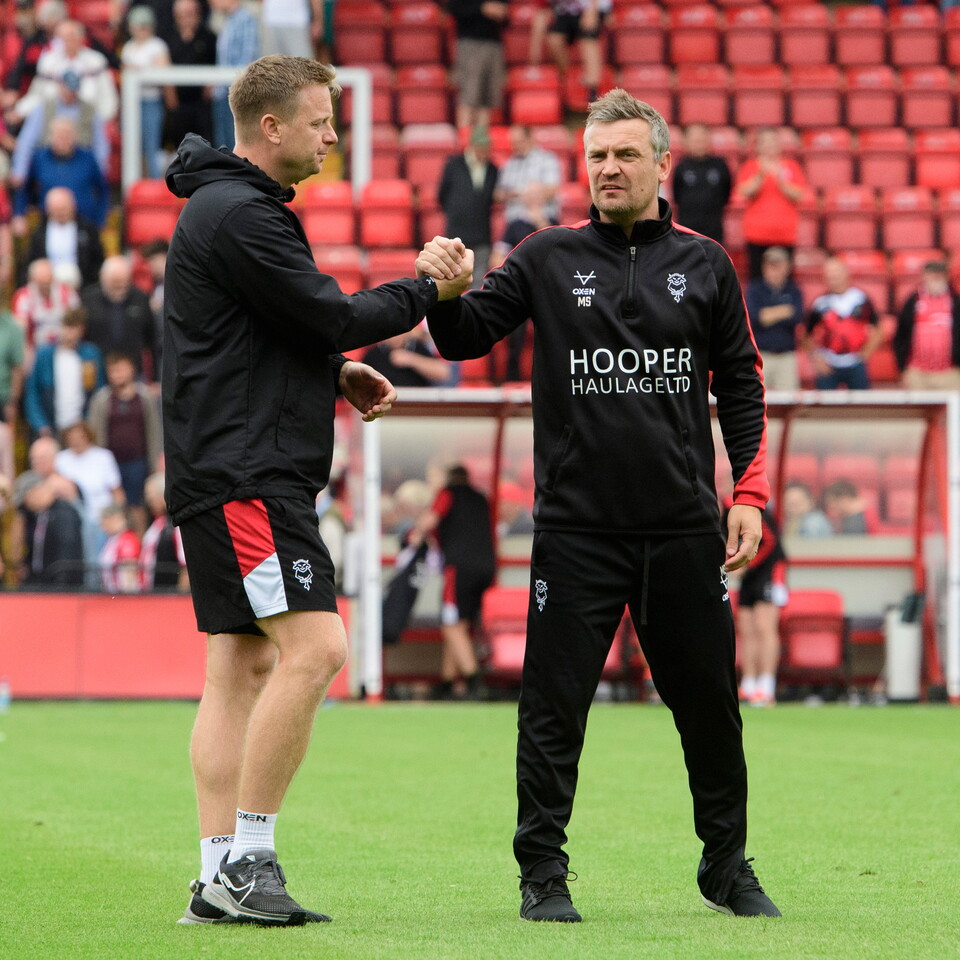 Tom Shaw and Michael Skubala shake hands while stood on a football pitch