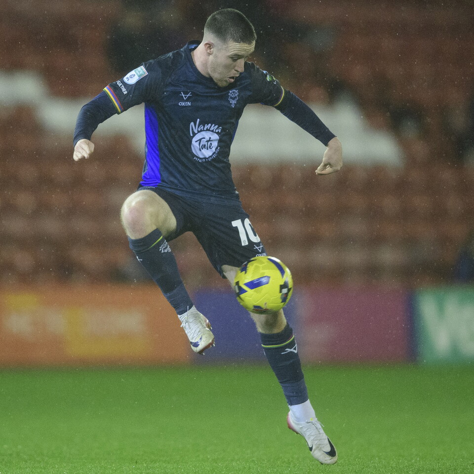Jack Moylan, wearing an all blue  kit, kicks the ball with his right foot