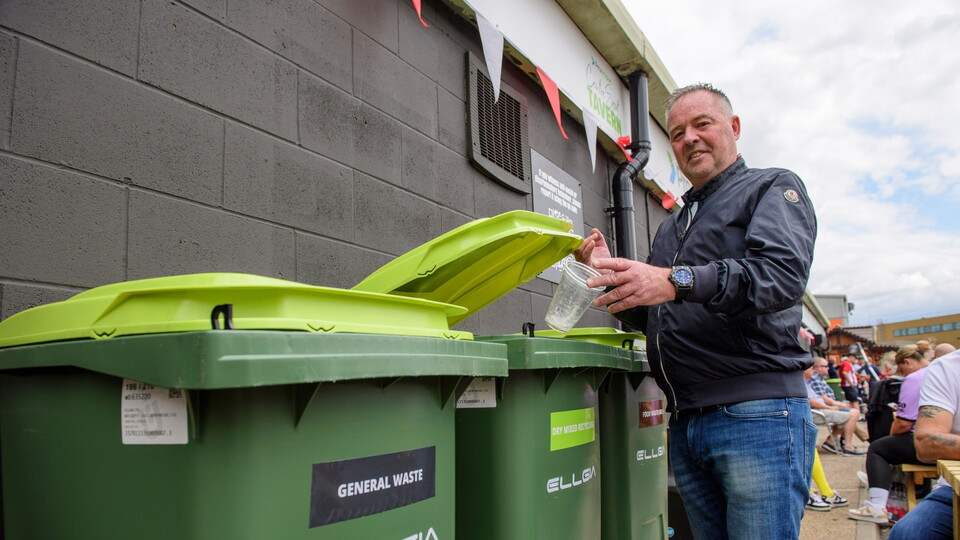 A supporters putting a plastic cup in a green Ellgia recycling bin.