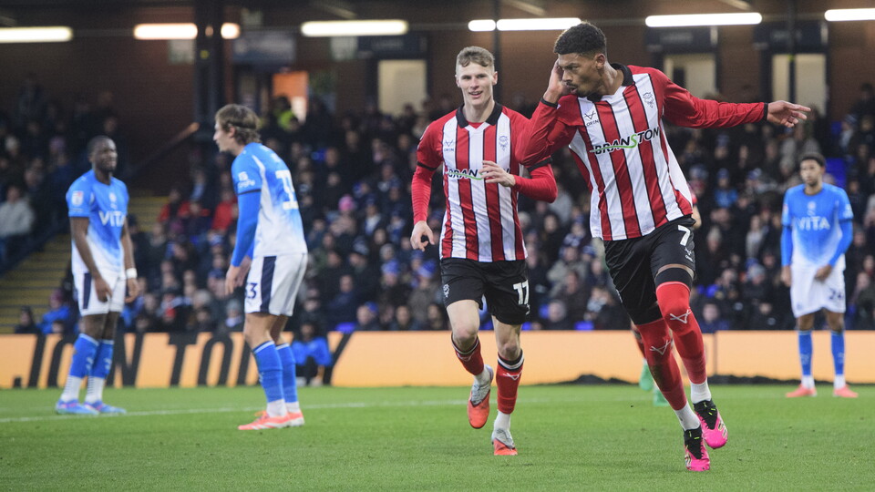 Rob Street and Reeco Hackett celebrate after scoring a goal. Both are wearing red and white striped tops and black shorts.