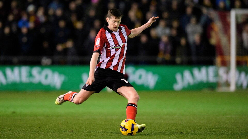 A man in a red and white striped shirt kicking a football. 