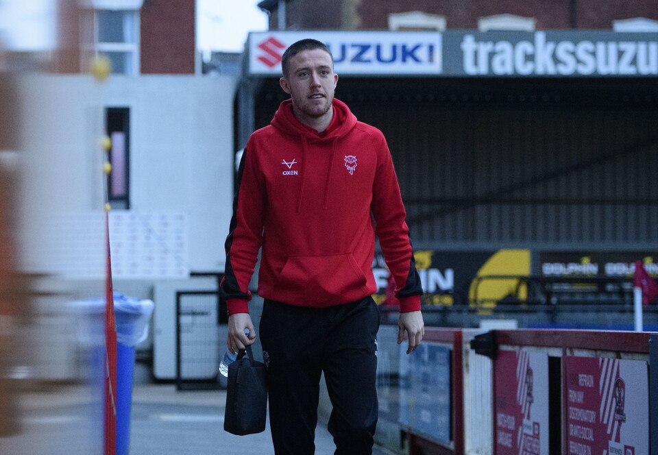 A man in a red hoody walks alongside a football pitch