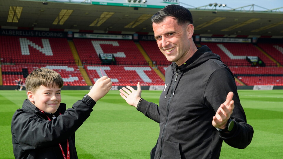 A young person shows a yellow card to a referee on a football pitch.  