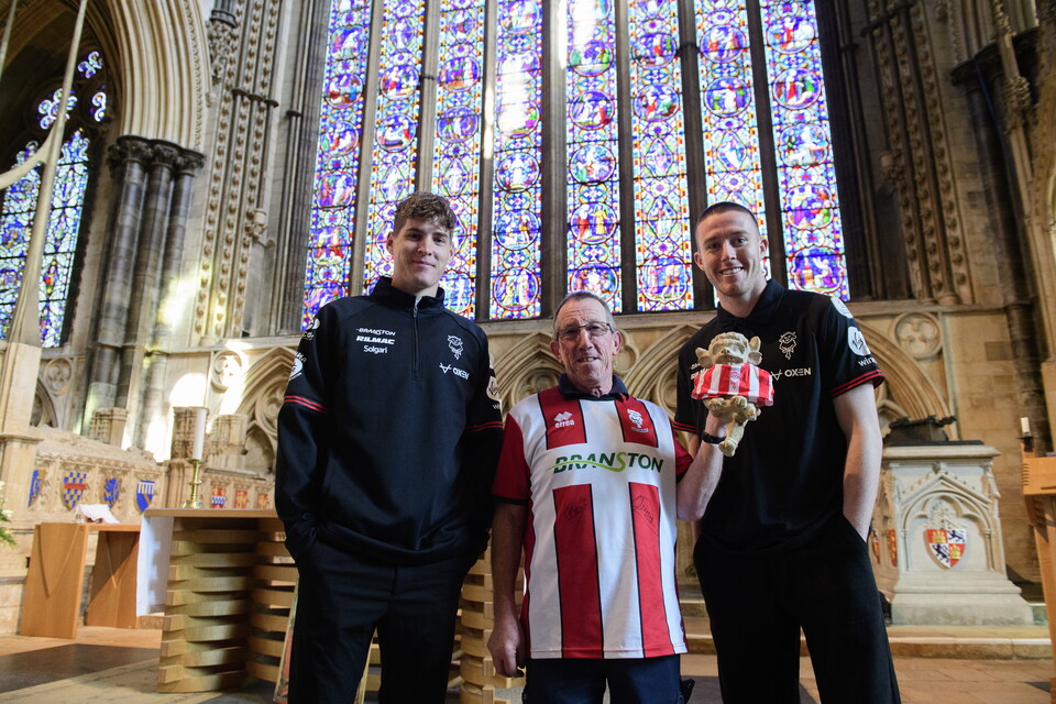 Ivan Varfolomeev, Stuart Boyfield and Jack Moylan hold a replica of the Lincoln Imp with a Lincoln City shirt attached to it.