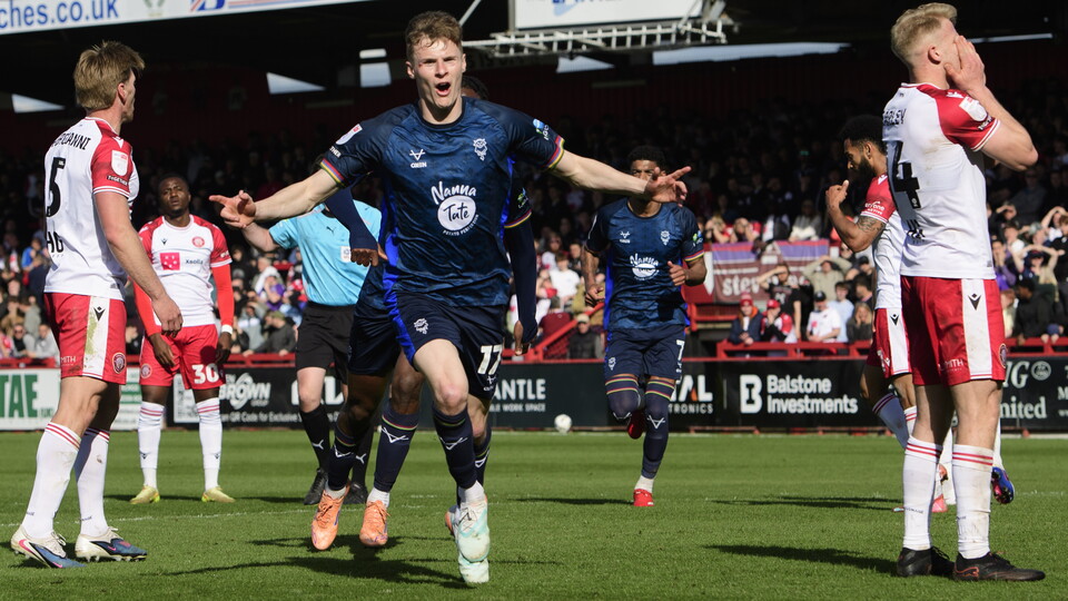 Rob Street celebrates after scoring for Lincoln City. He is wearing an all blue kit and holding his arms out.