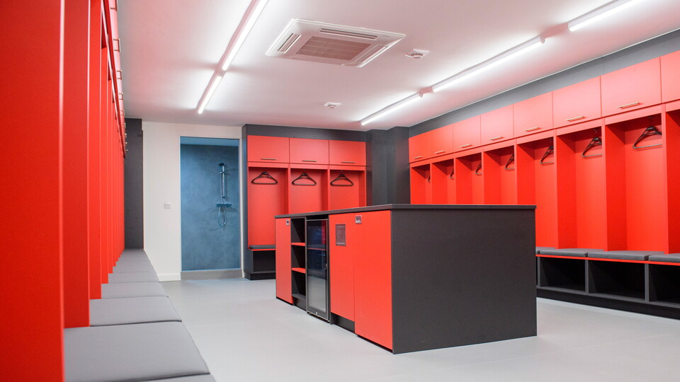 A red changing room with an island unit which features fridges and laundry bins.
