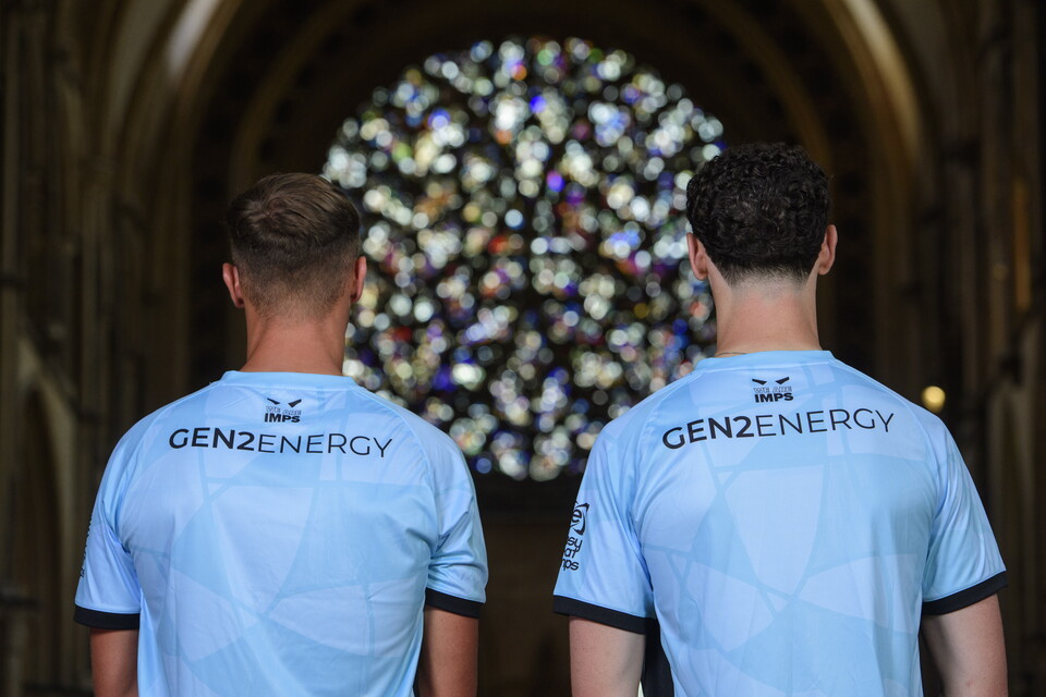 The backs of two people in blue football tops, with a stained glass window in the background. "Gen2 Energy" is on the back of each shirt.