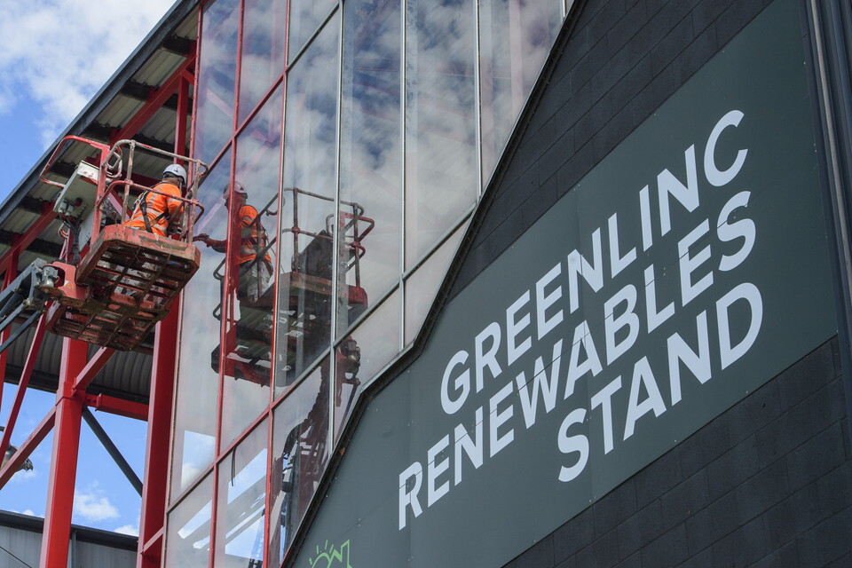 A man on a cherrypicker paints a football stand