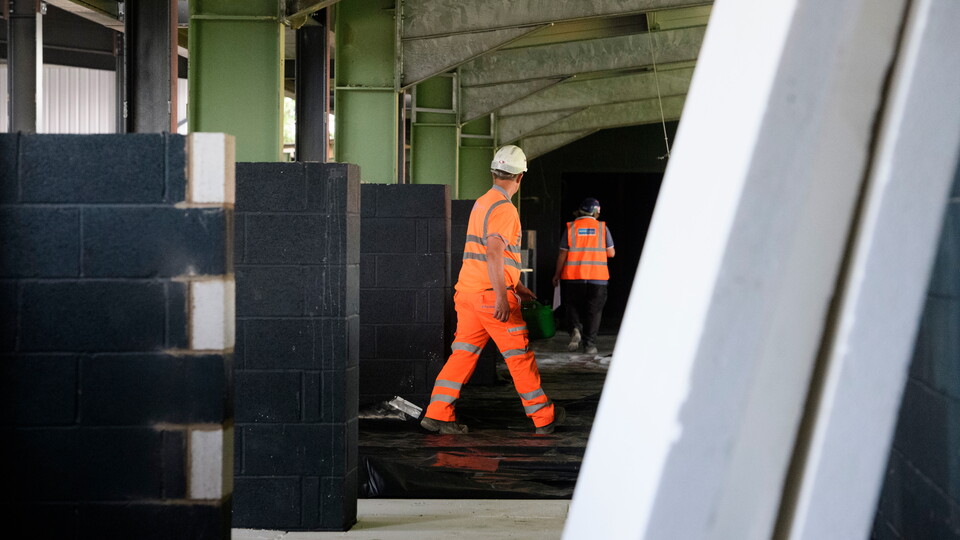 A workman in hi-vis and a hard hat walks through a building site