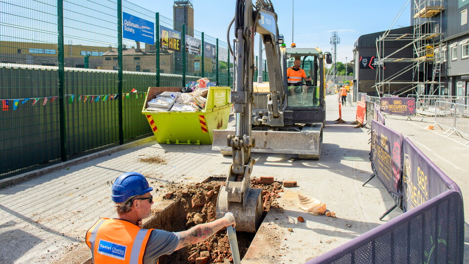 Workmen using a digger to work on trenching in a road